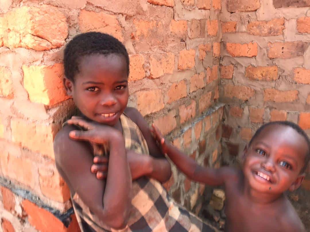 Two young children stand inside the brick walls of Granny Angella's unfinished new house.