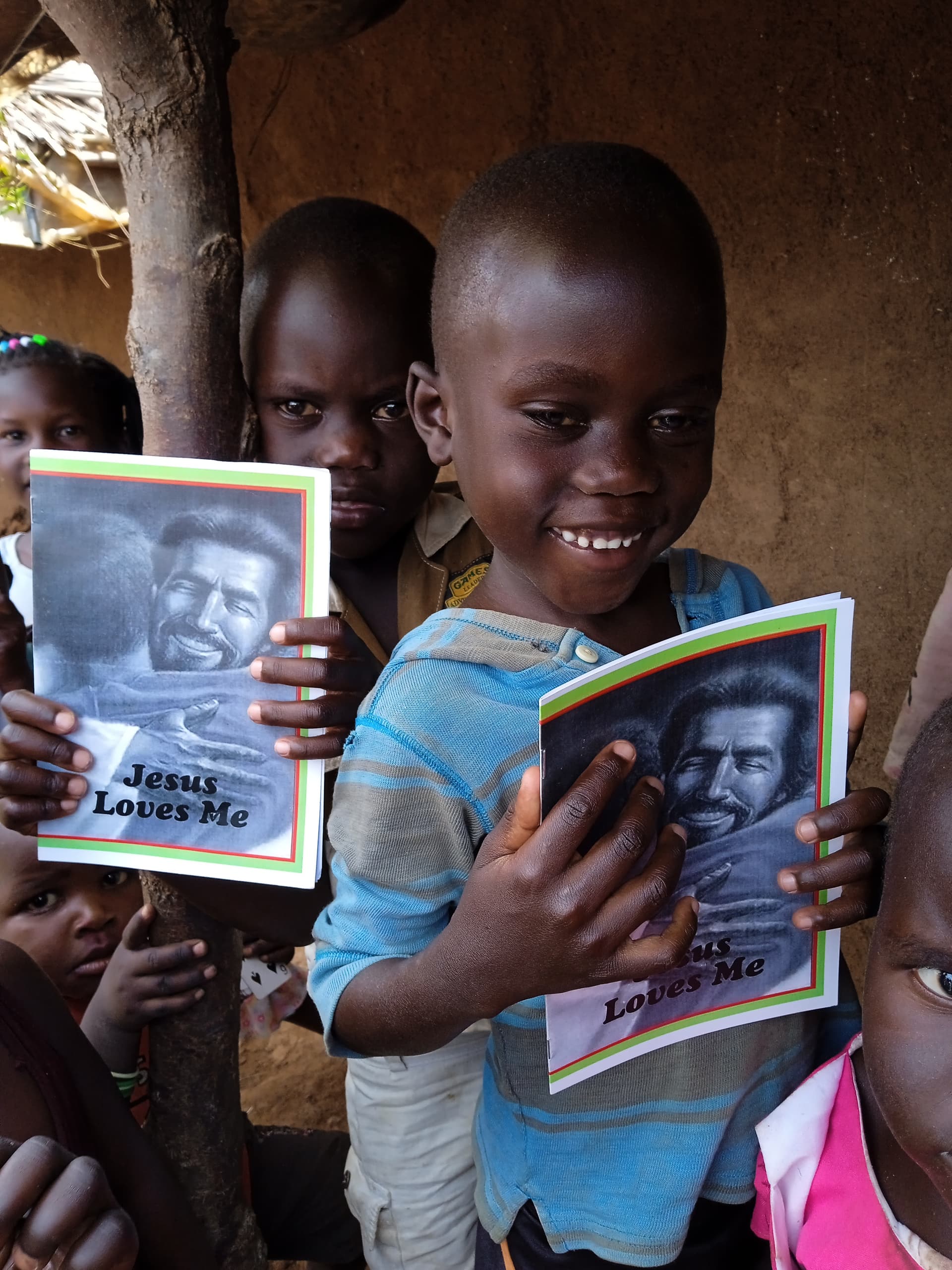 Children stand together holding photographs and food gift items.