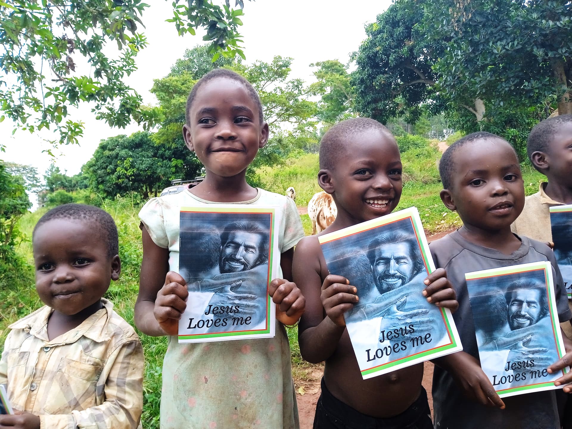 Three children stand outdoors along a road holding photographs.