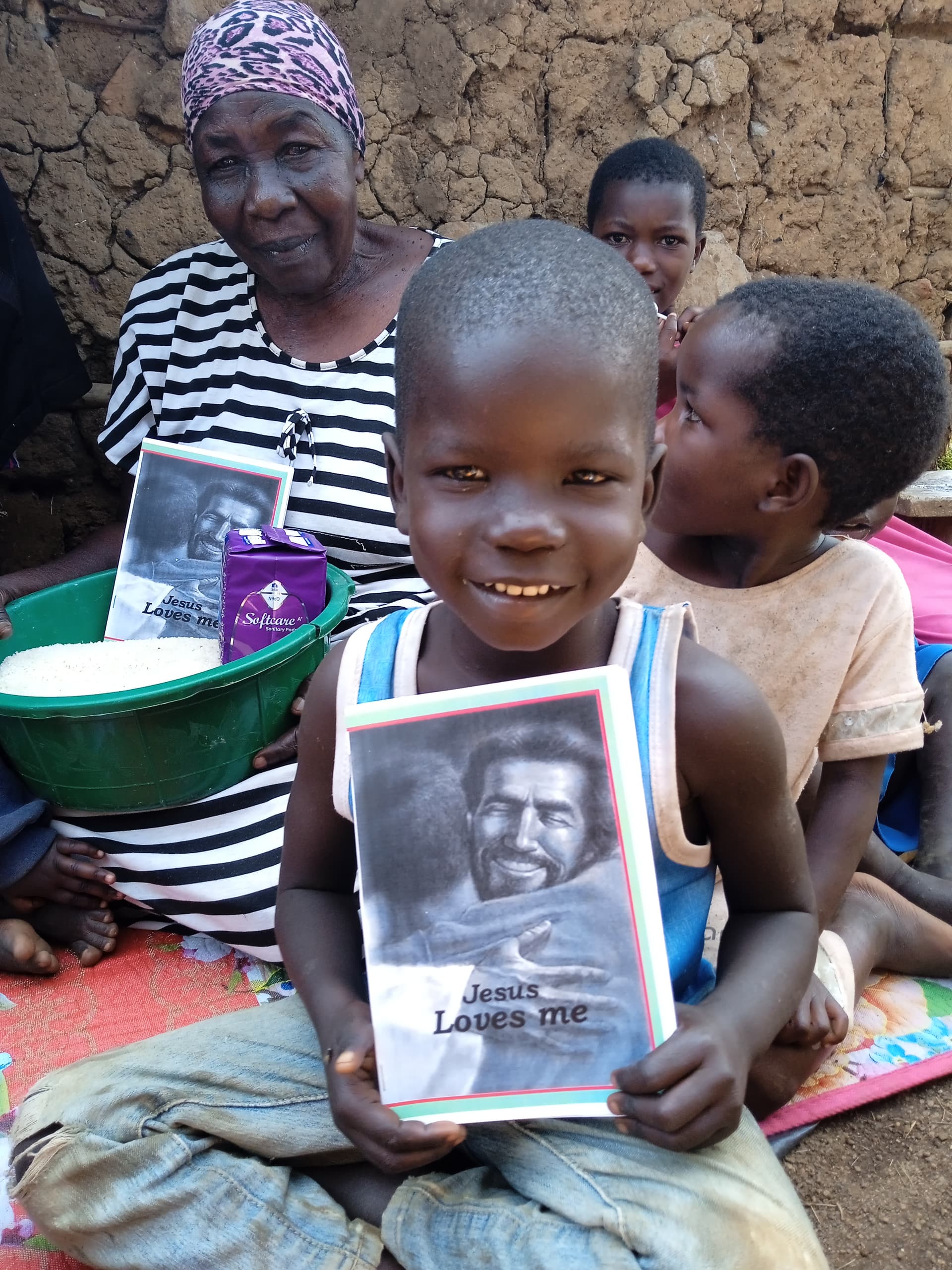 An elderly woman in a striped dress sits with children, holding a photograph beside a green basin.
