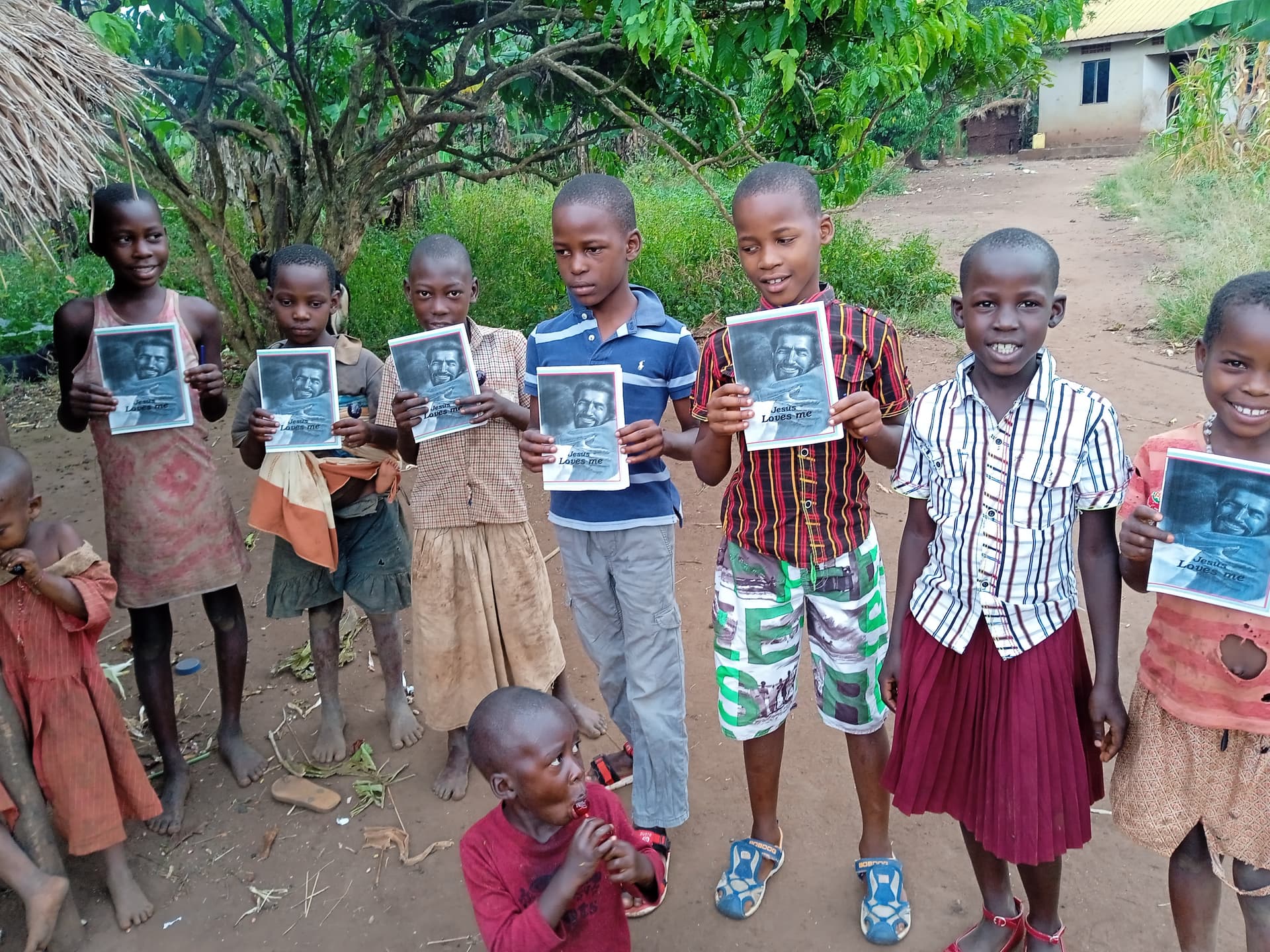 Group of children outdoors raise their hands and cheer, some holding a photo booklet, in an open field.