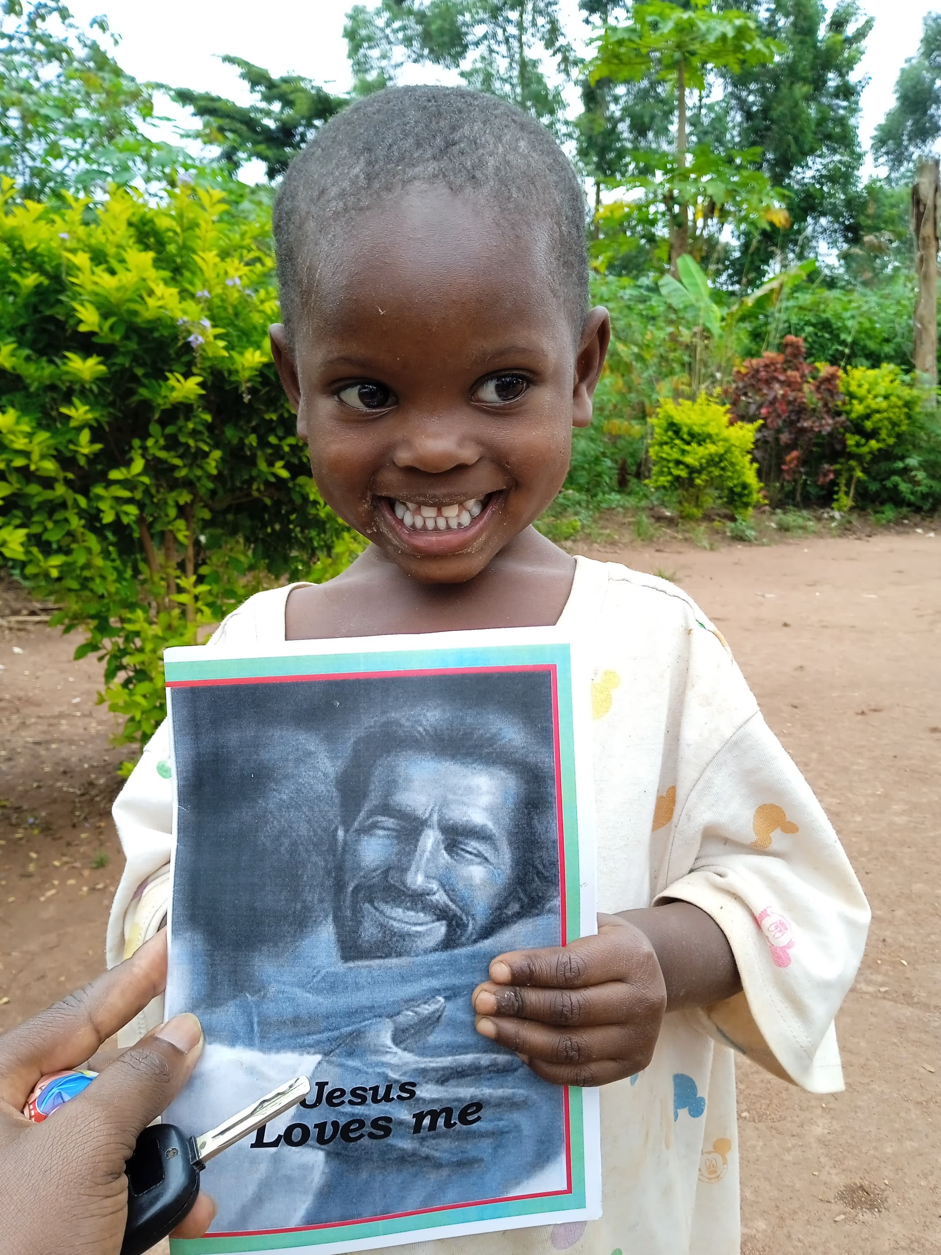 Girl smiling outdoors near flowering plants, holding a gospel tract booklet.