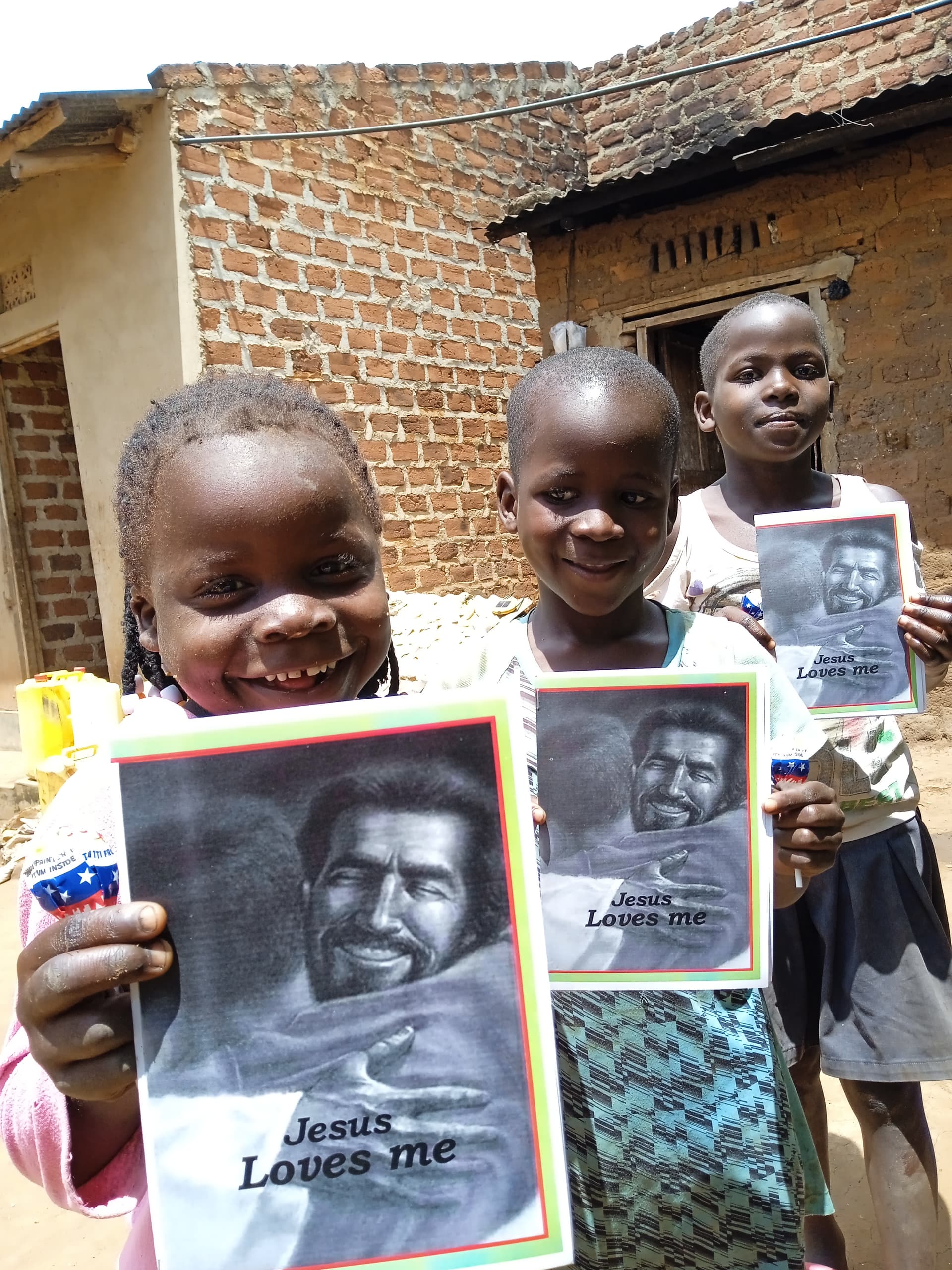 Two children standing outside a mud home, one holding a gospel tract booklet.