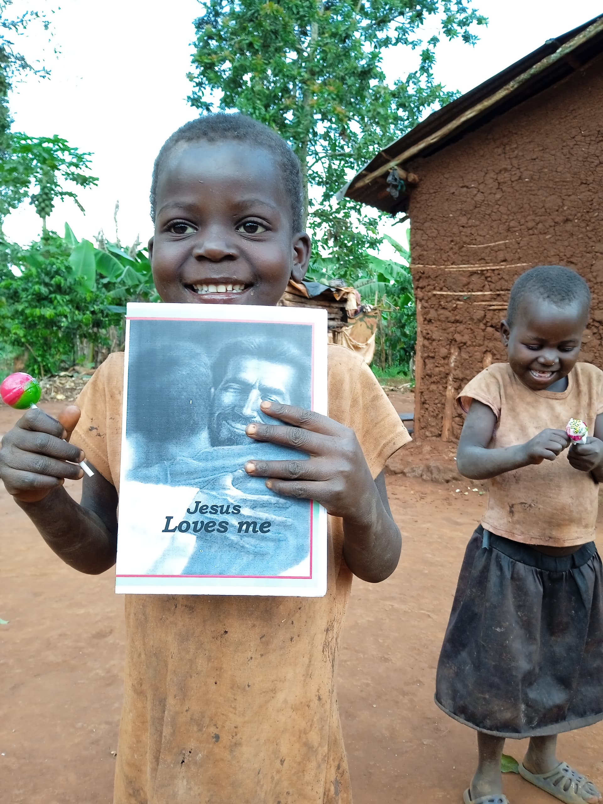 Girl smiling outdoors, holding a gospel tract booklet beside another child.
