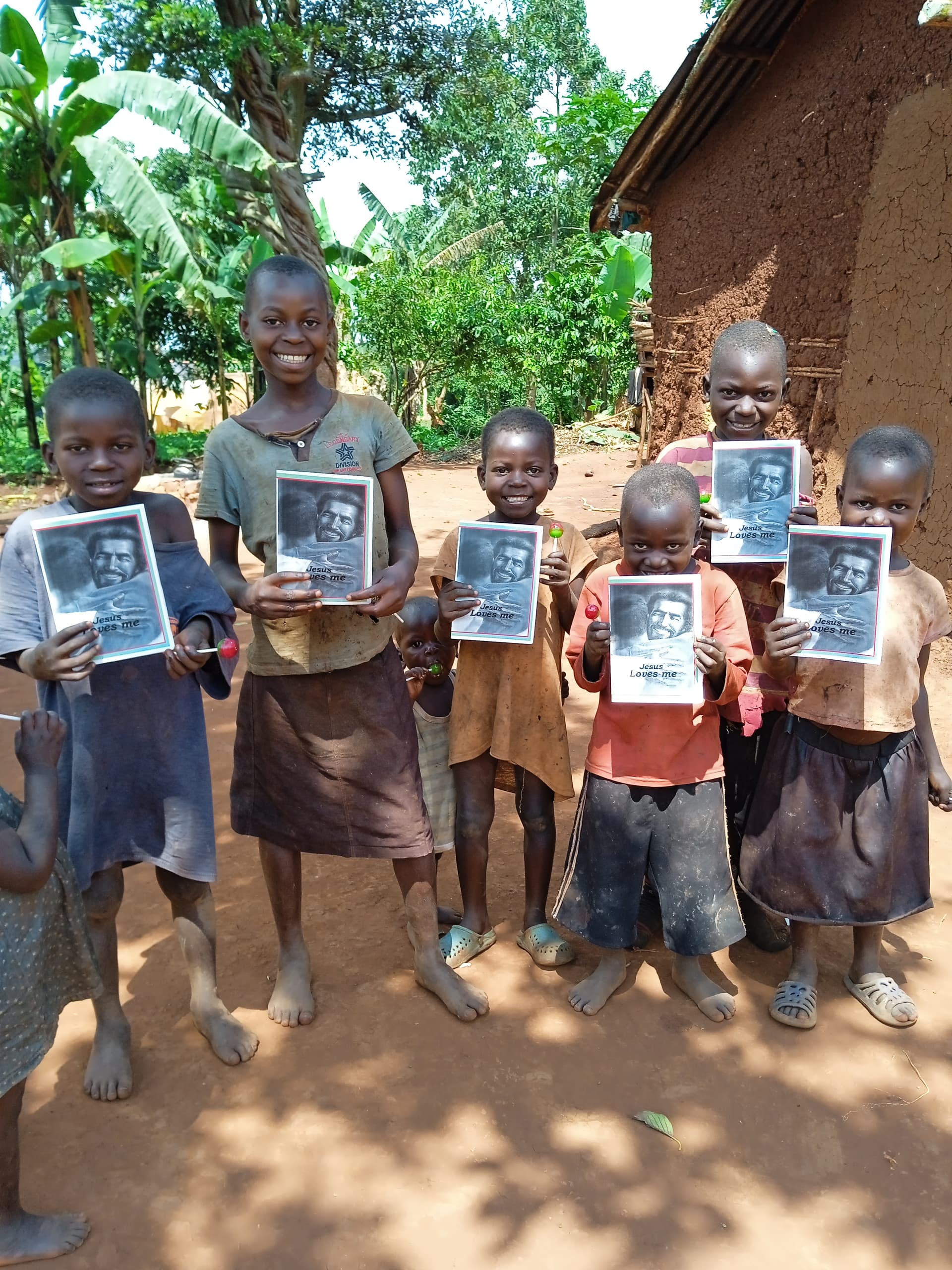 Group of children standing together outside a mud home, each holding a gospel tract booklet.