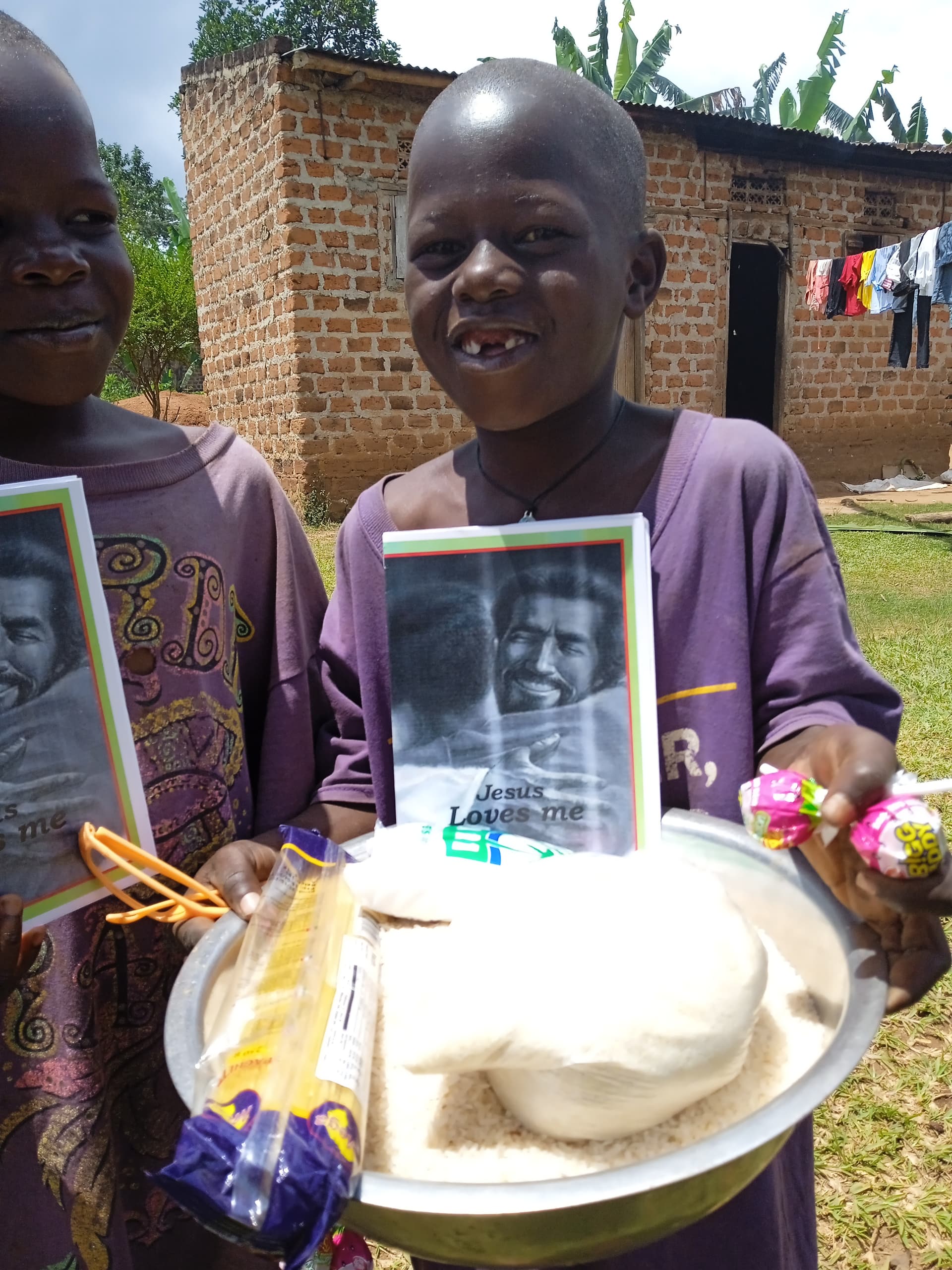 Two girls standing together at a brick home, one holding a tract booklet and food bowl.