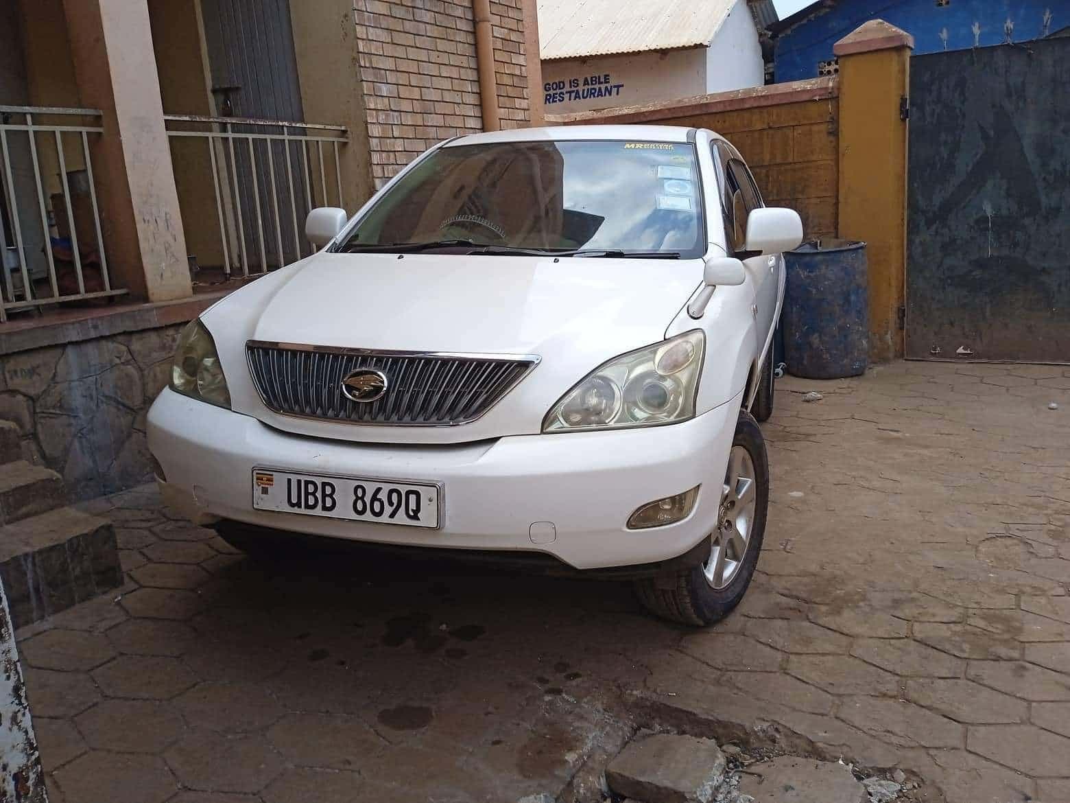 White SUV with a Ugandan license plate parked in a driveway, JFM's newly purchased vehicle.