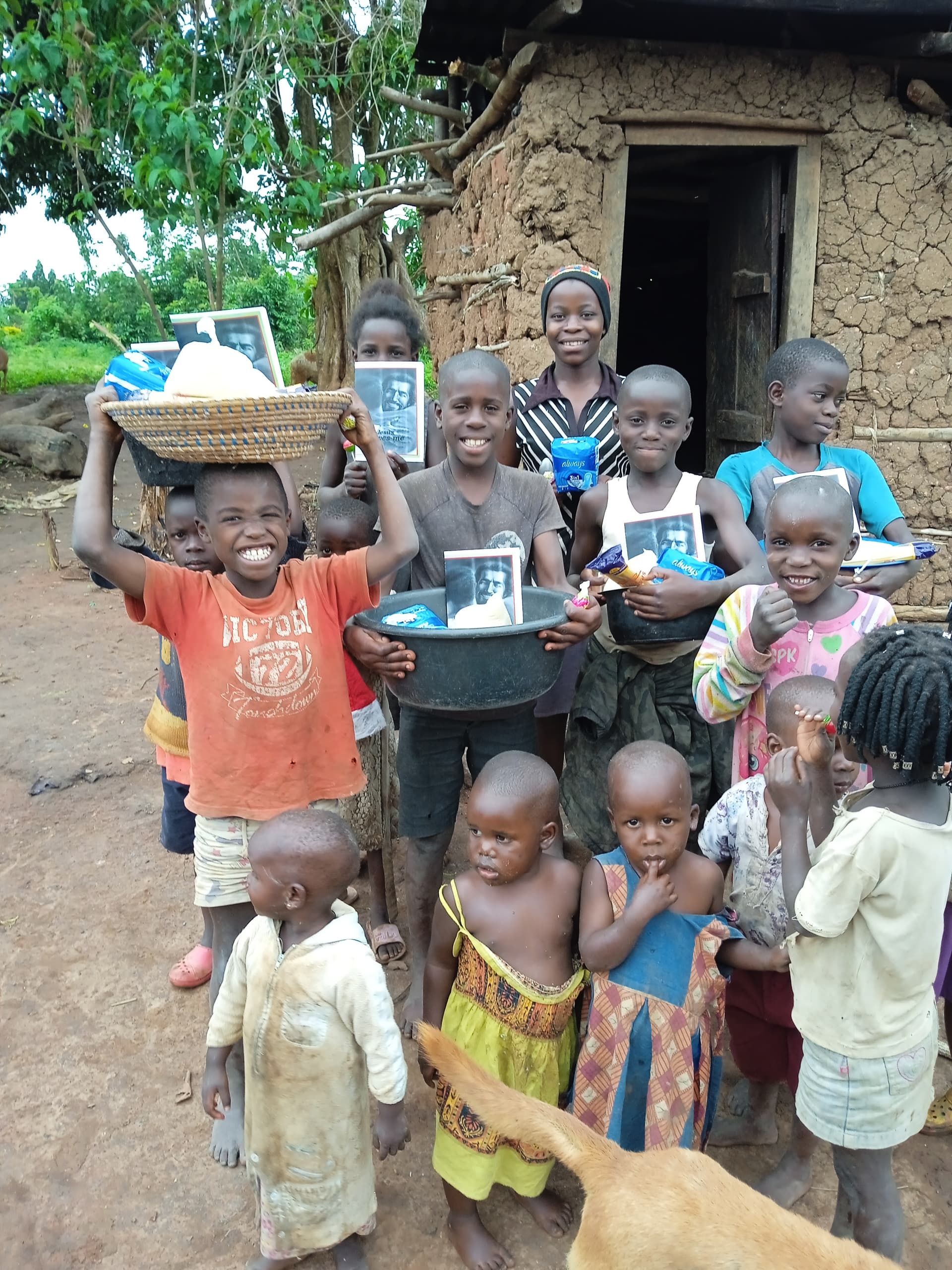 Group of children outside a mud-brick home, one boy holding a basin of JFM food gifts.