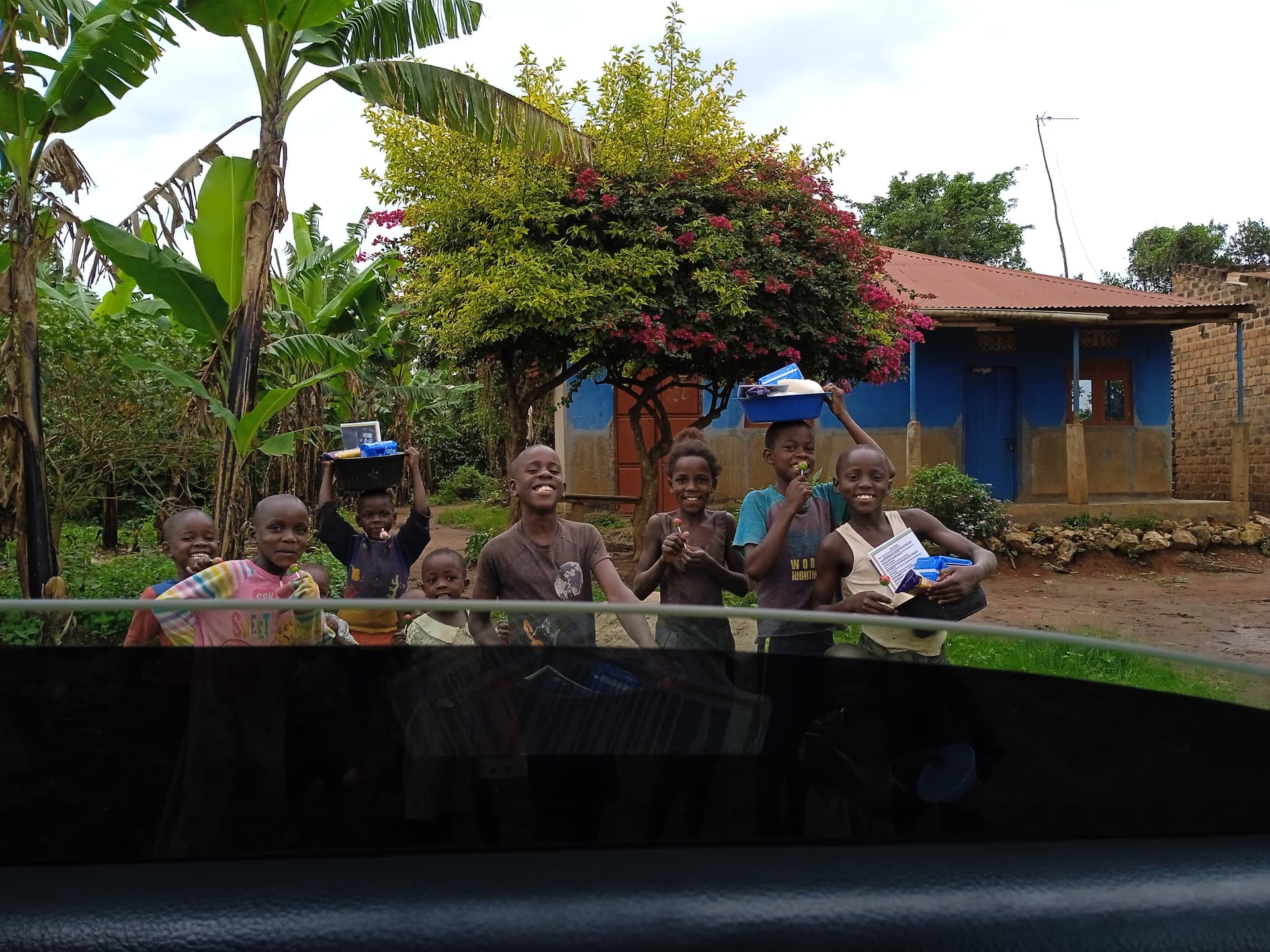 Photo taken through a vehicle windshield showing a group of people gathered outside a house.