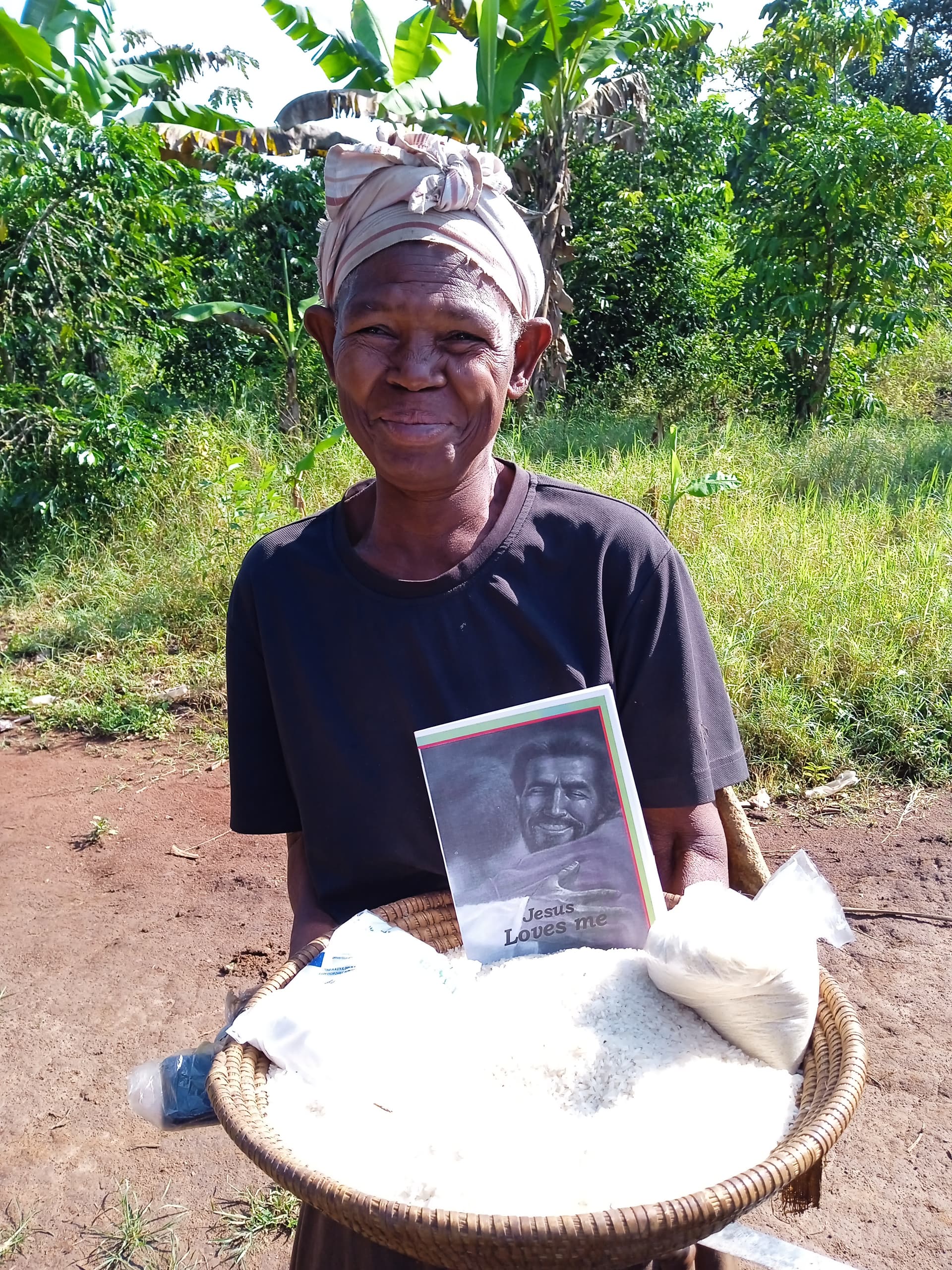 Woman in a headscarf holds a printed photo card over a basket of rice she received as a food gift.