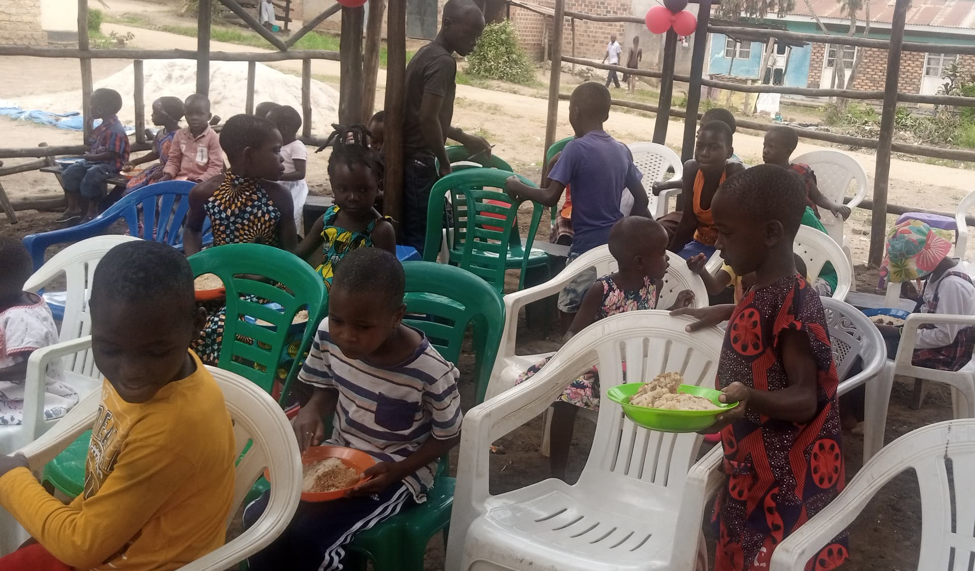 Congregation seated in white plastic chairs under a balloon-decorated tent at Amazing Grace Church.