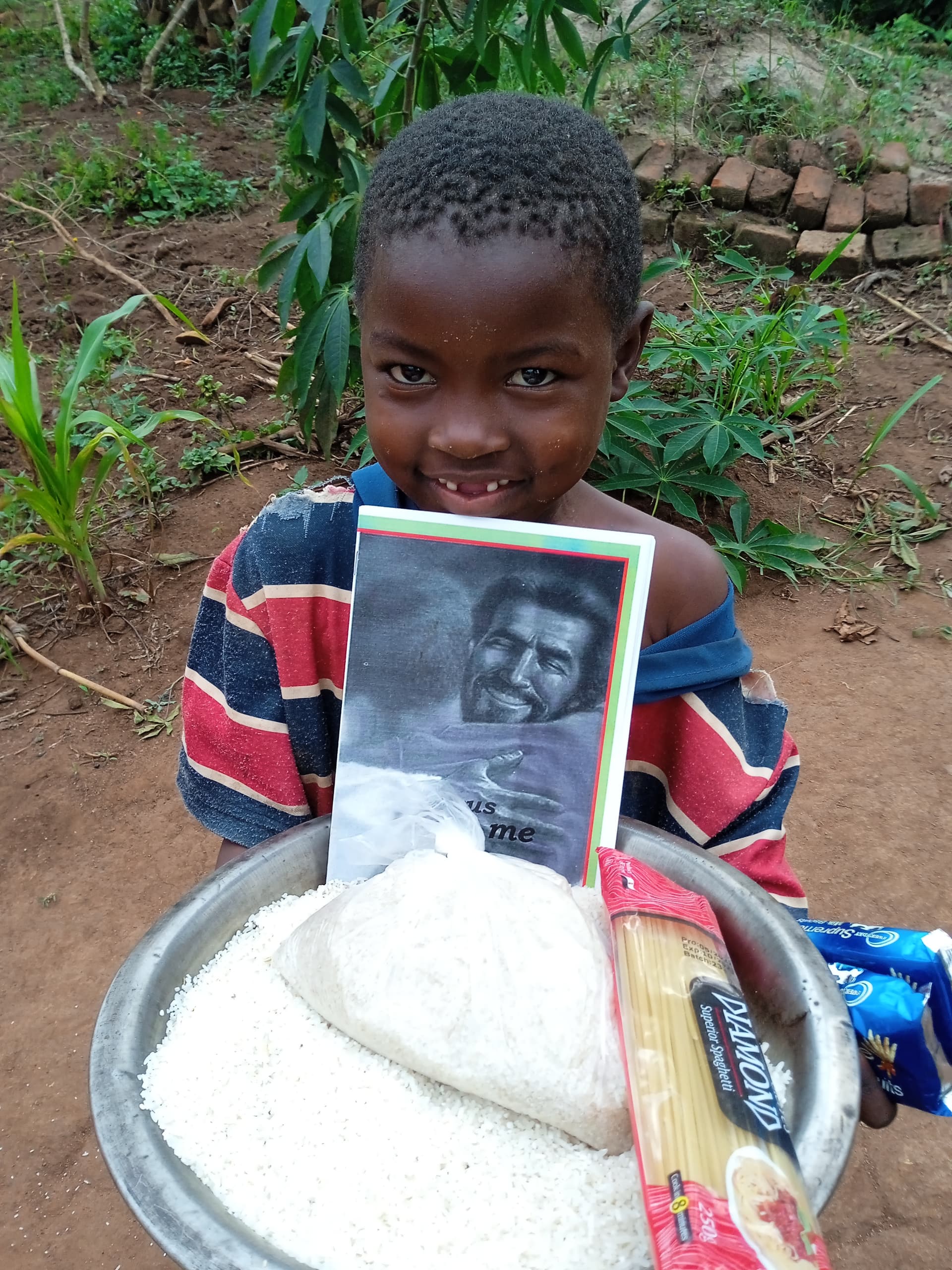 Boy smiling and holding a plate of rice along with a photo card outdoors.