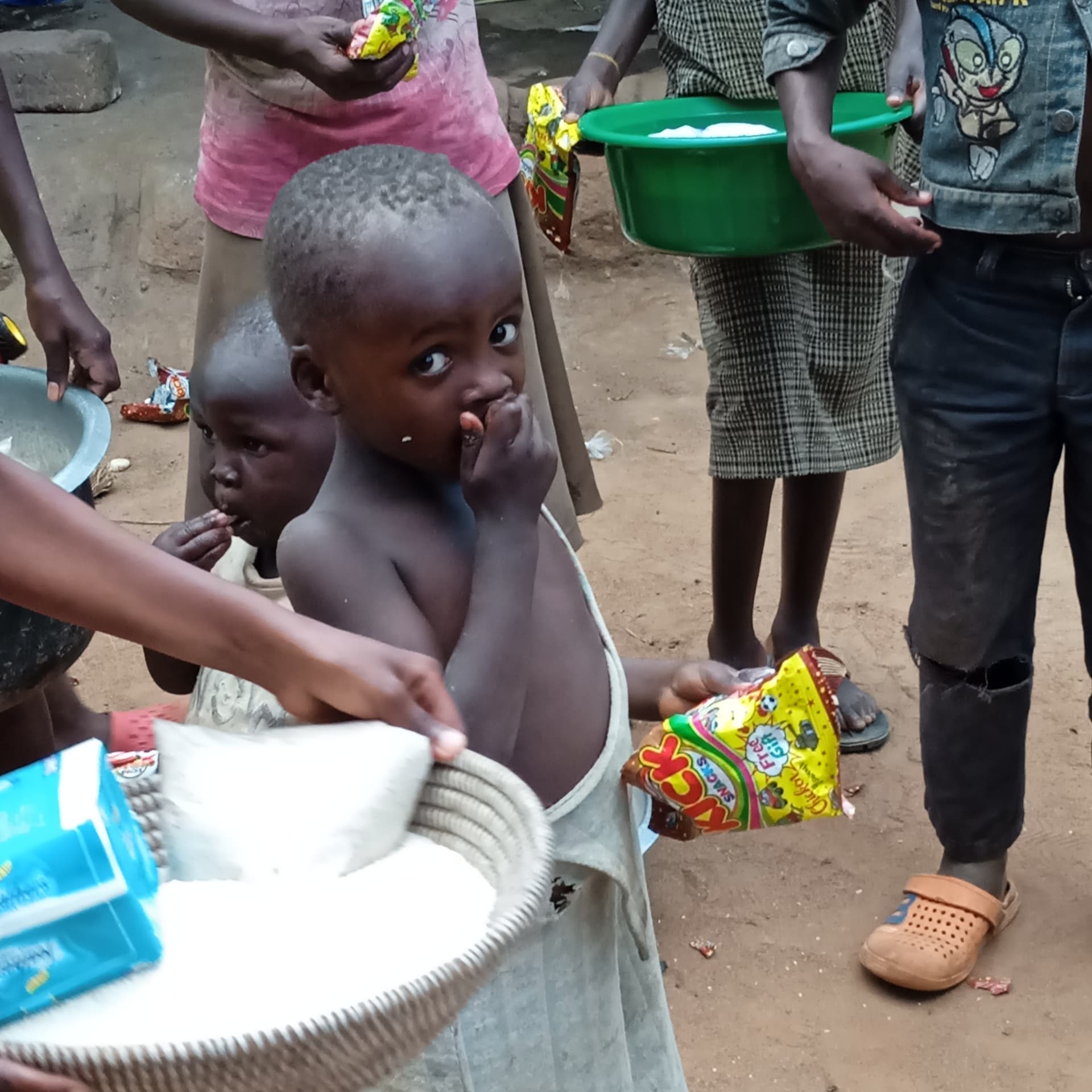 Children hold basins and food packages, one carrying a green basin on her head.