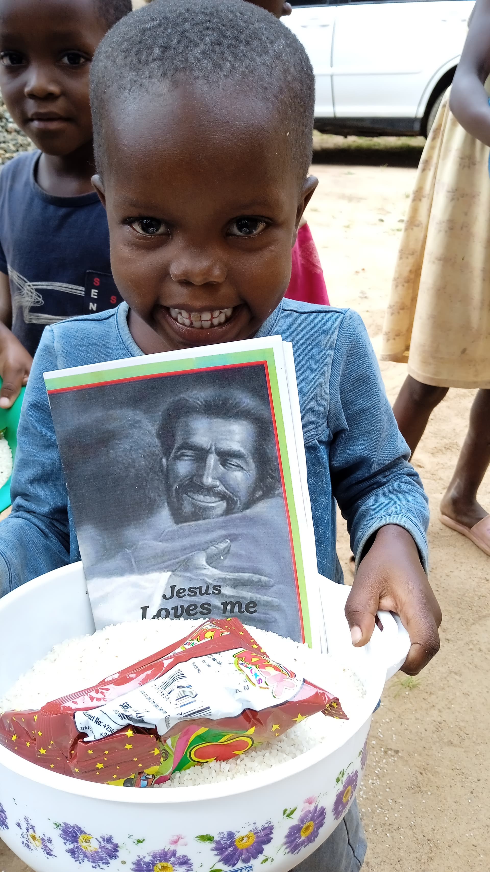 Young boy holds a metal basin containing a photo card and food items.