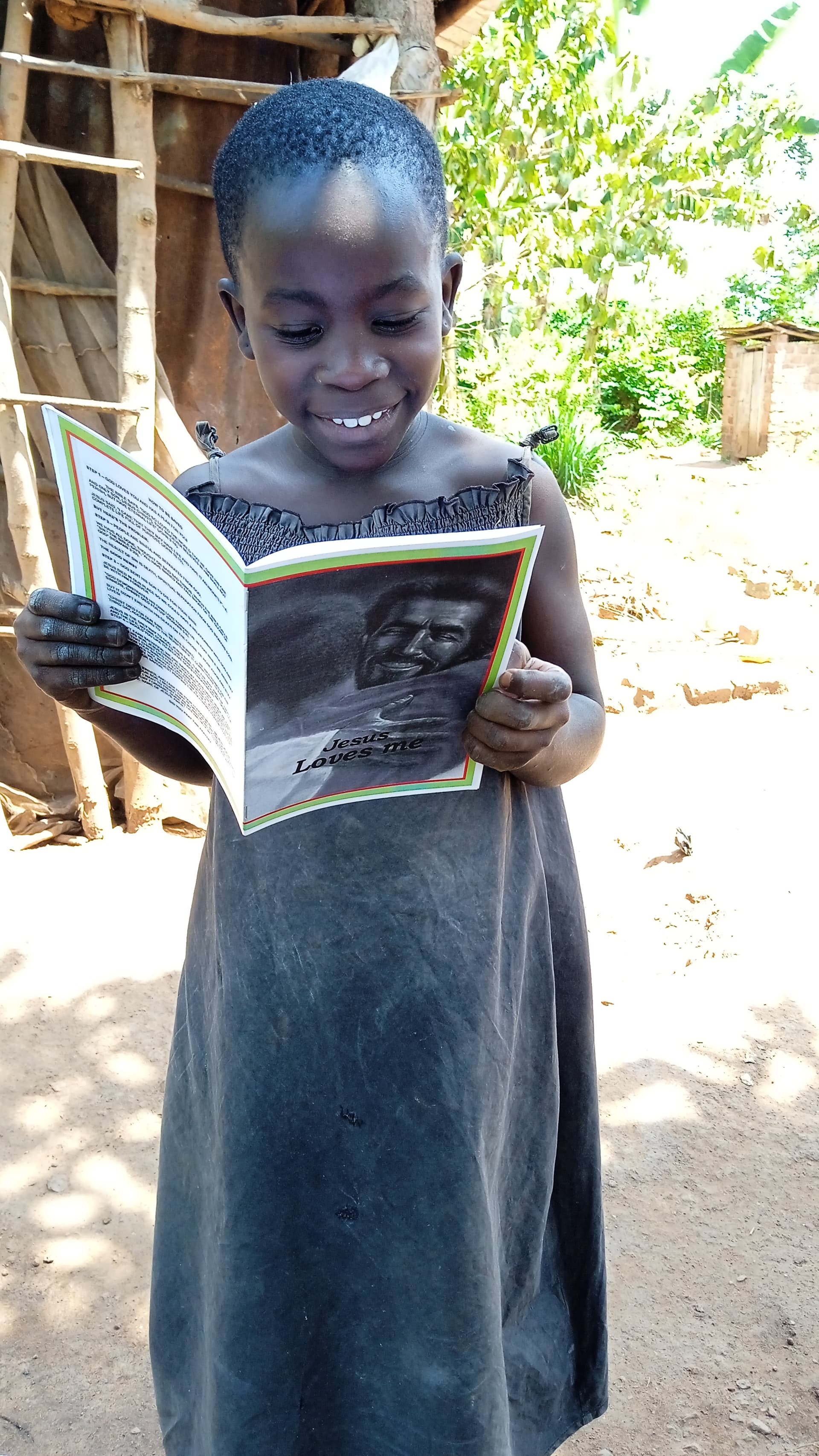 Young girl in a blue dress smiles while reading an open picture book outdoors.