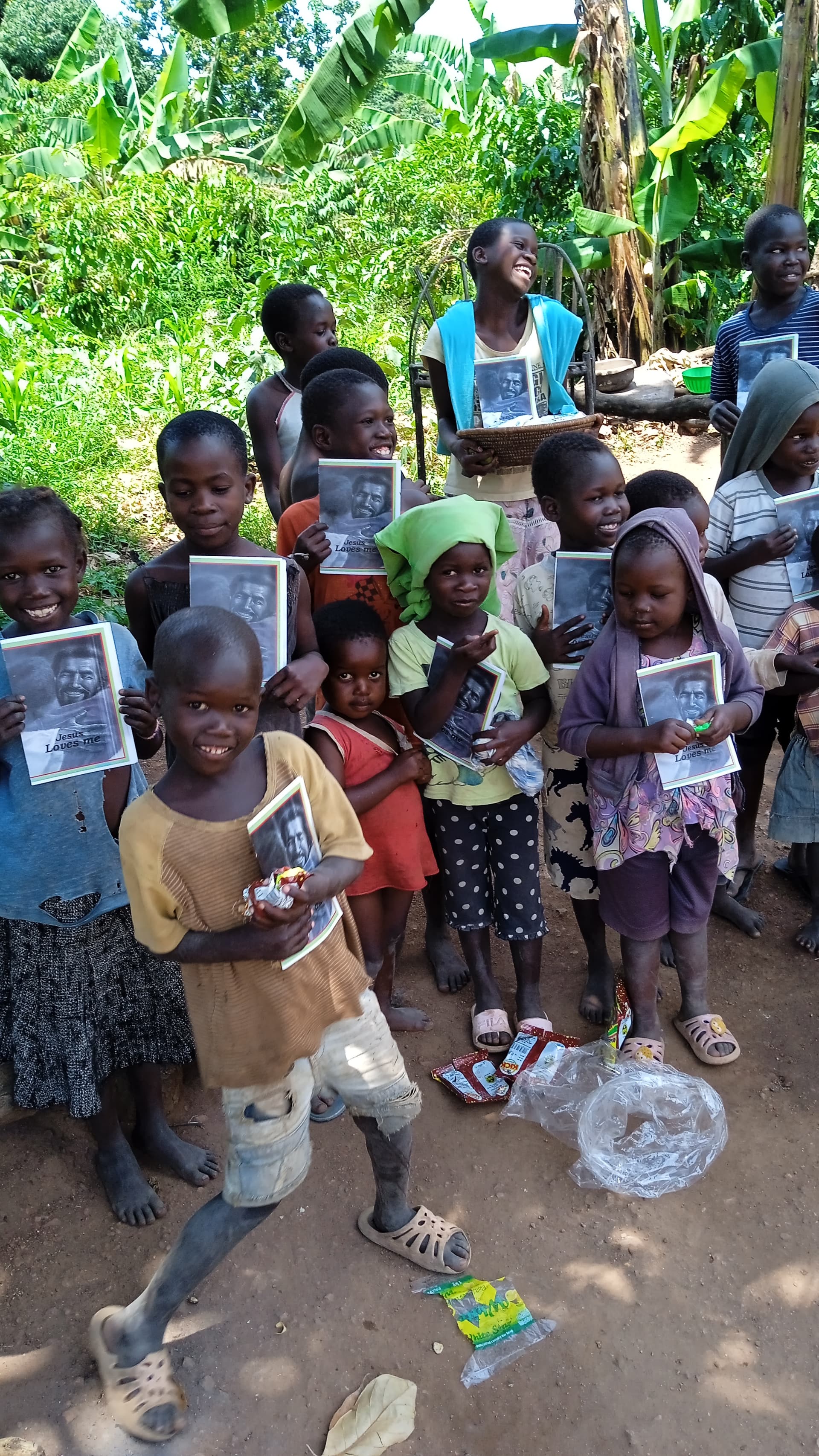Group of children gathered outdoors, one in front holding a photo card and food basin.