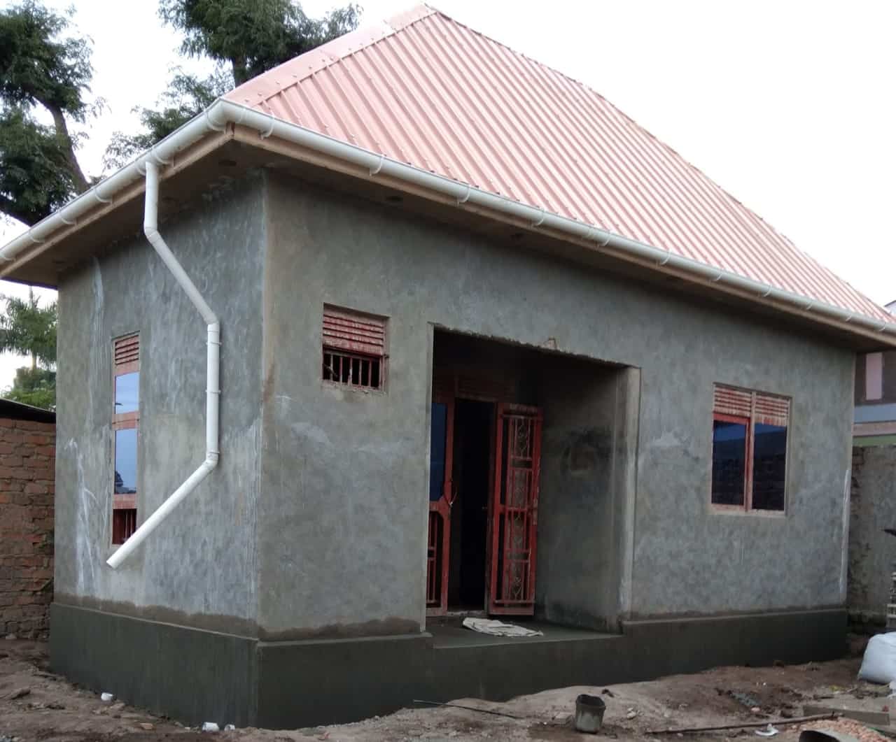 Newly built small house with a red metal roof and cement-plastered walls at the church backyard.