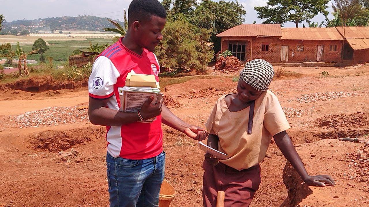 JFM staff member in a red shirt walks with a quarry worker near a brick building at the site.