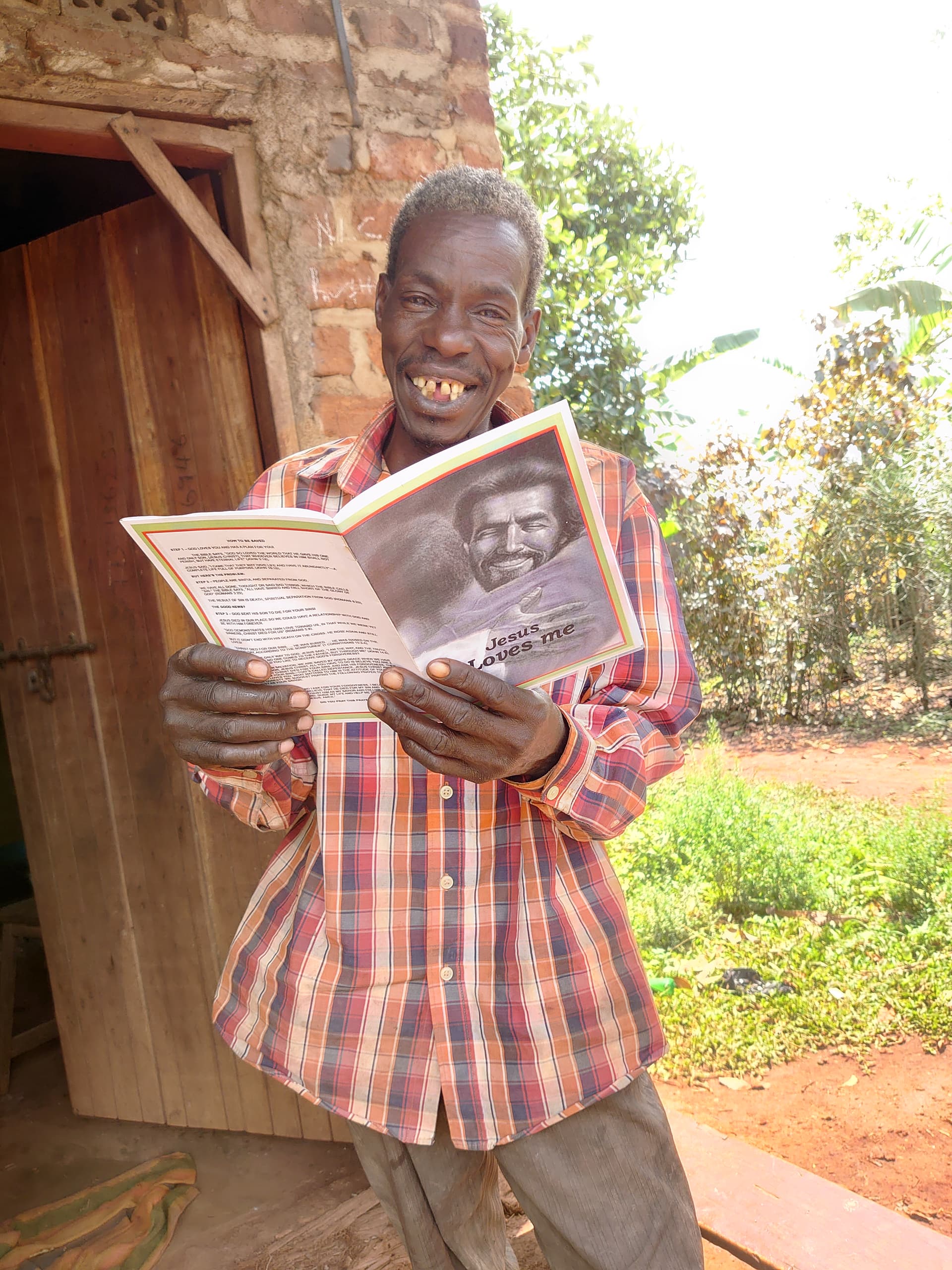 A child stands outdoors holding a gospel tract booklet near a wooden structure.