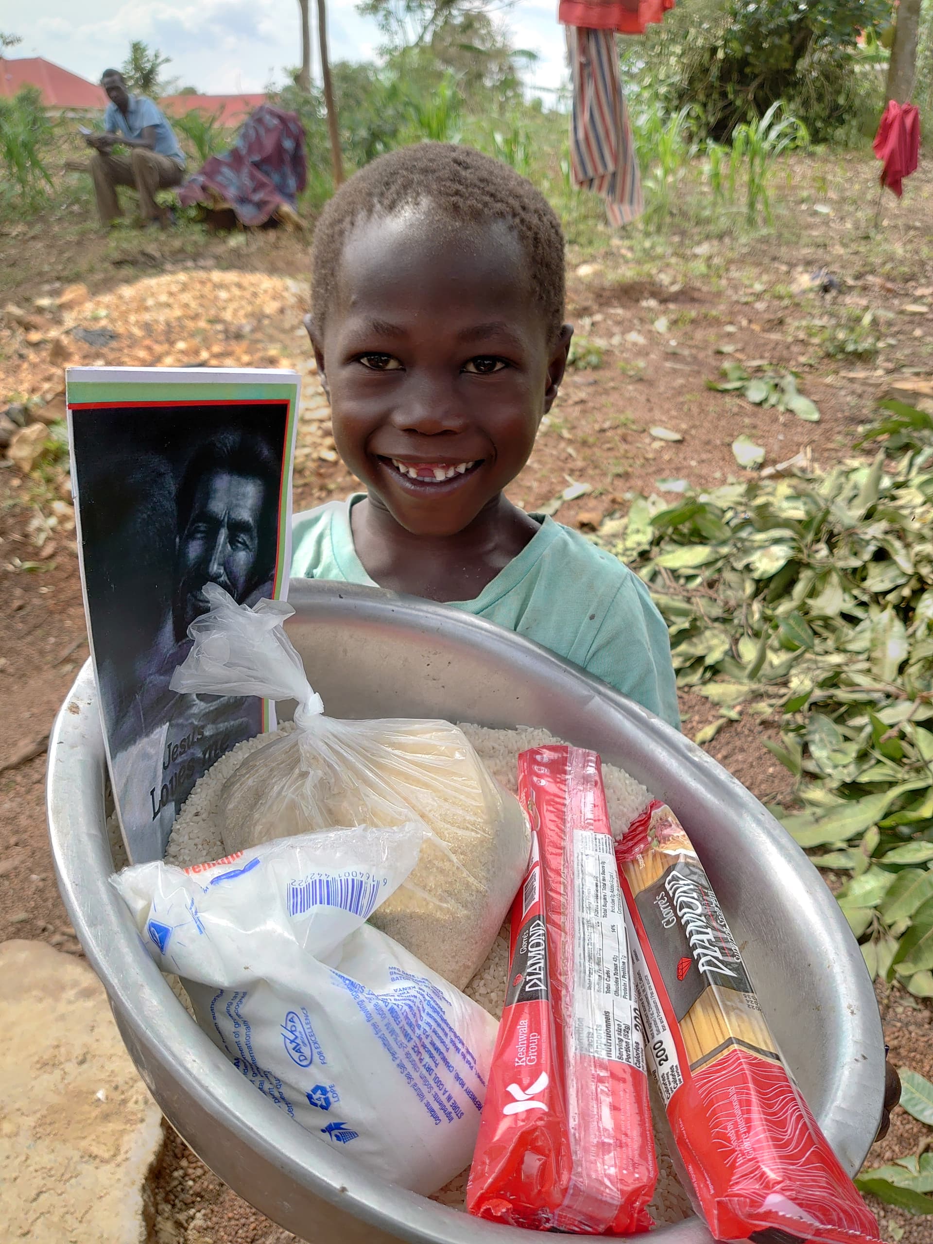 A child sits on the ground holding a basin with a food bag and gospel tract.