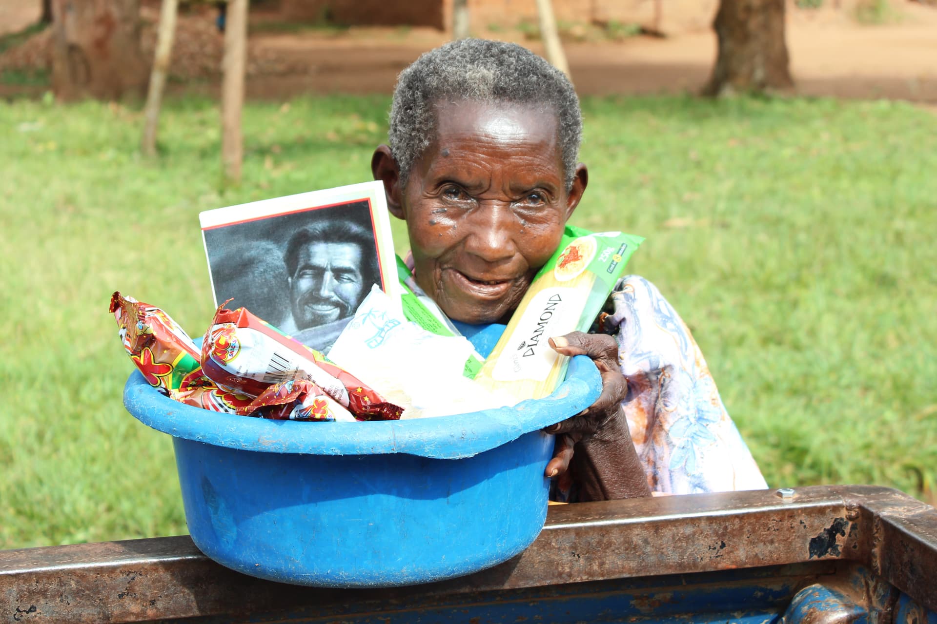 Elderly woman leaning over a blue basin filled with a food package and gift items.