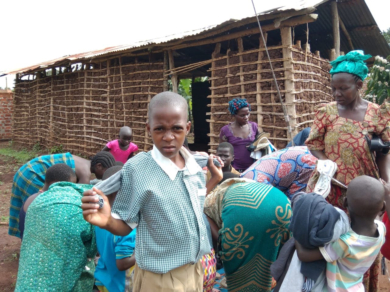 Elderly woman in a green head wrap and children gathered outside a thatched-roof mud building receiving donations.