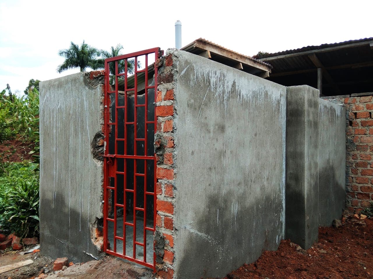 A newly constructed concrete-block latrine with a red metal door at the children's home grounds.