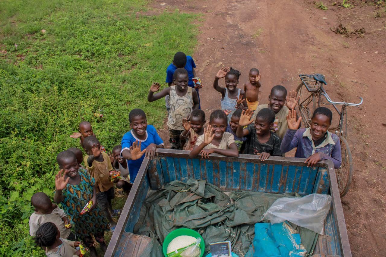 Overhead view of children seated in the bed of a blue pickup truck being transported to a distant village.