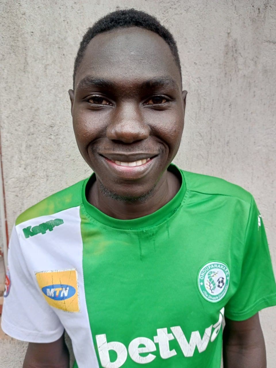 Headshot of a smiling young man wearing a green sponsored soccer jersey.