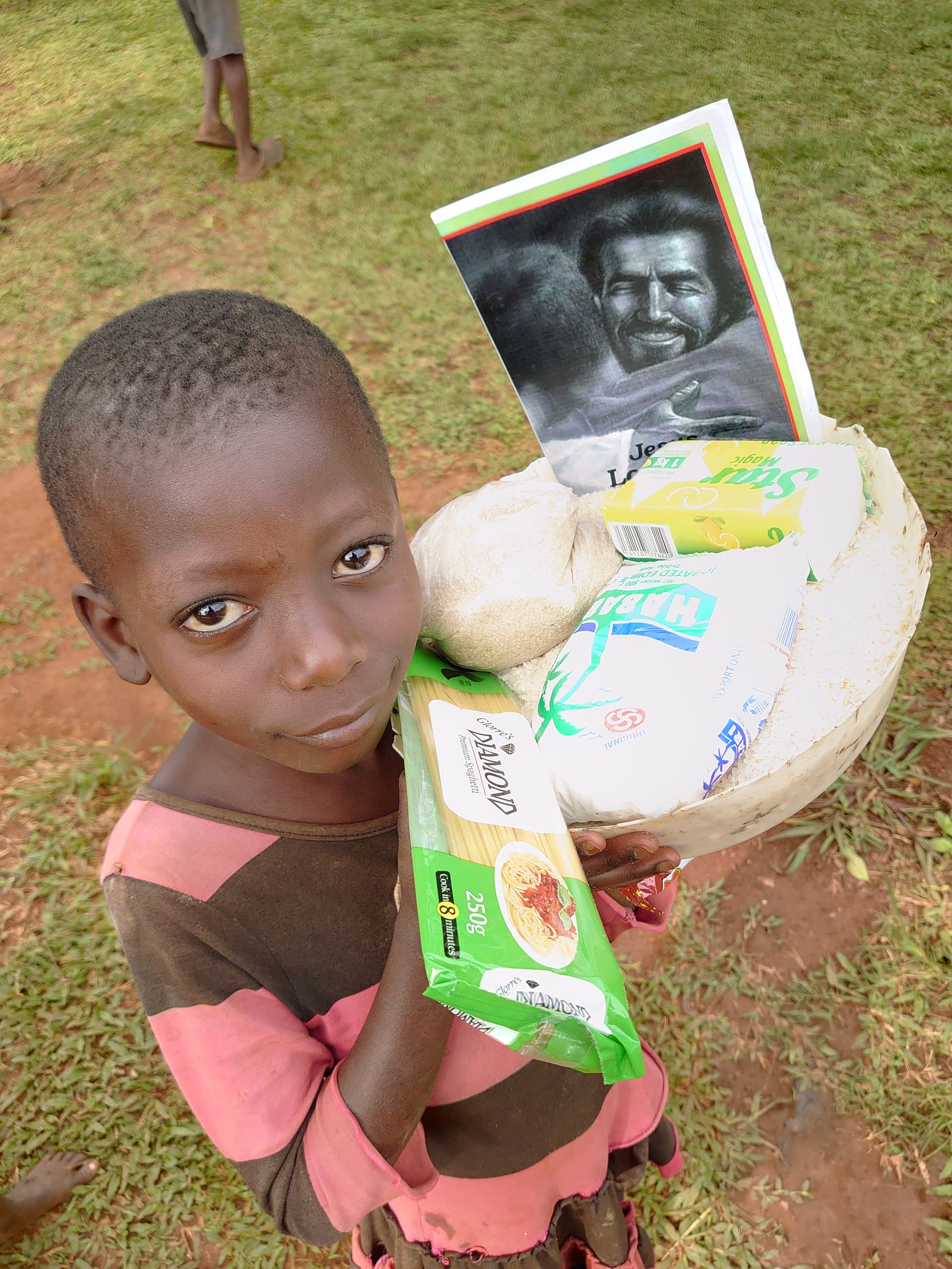 Child on dirt ground holding a food package with a photo insert and a green item.