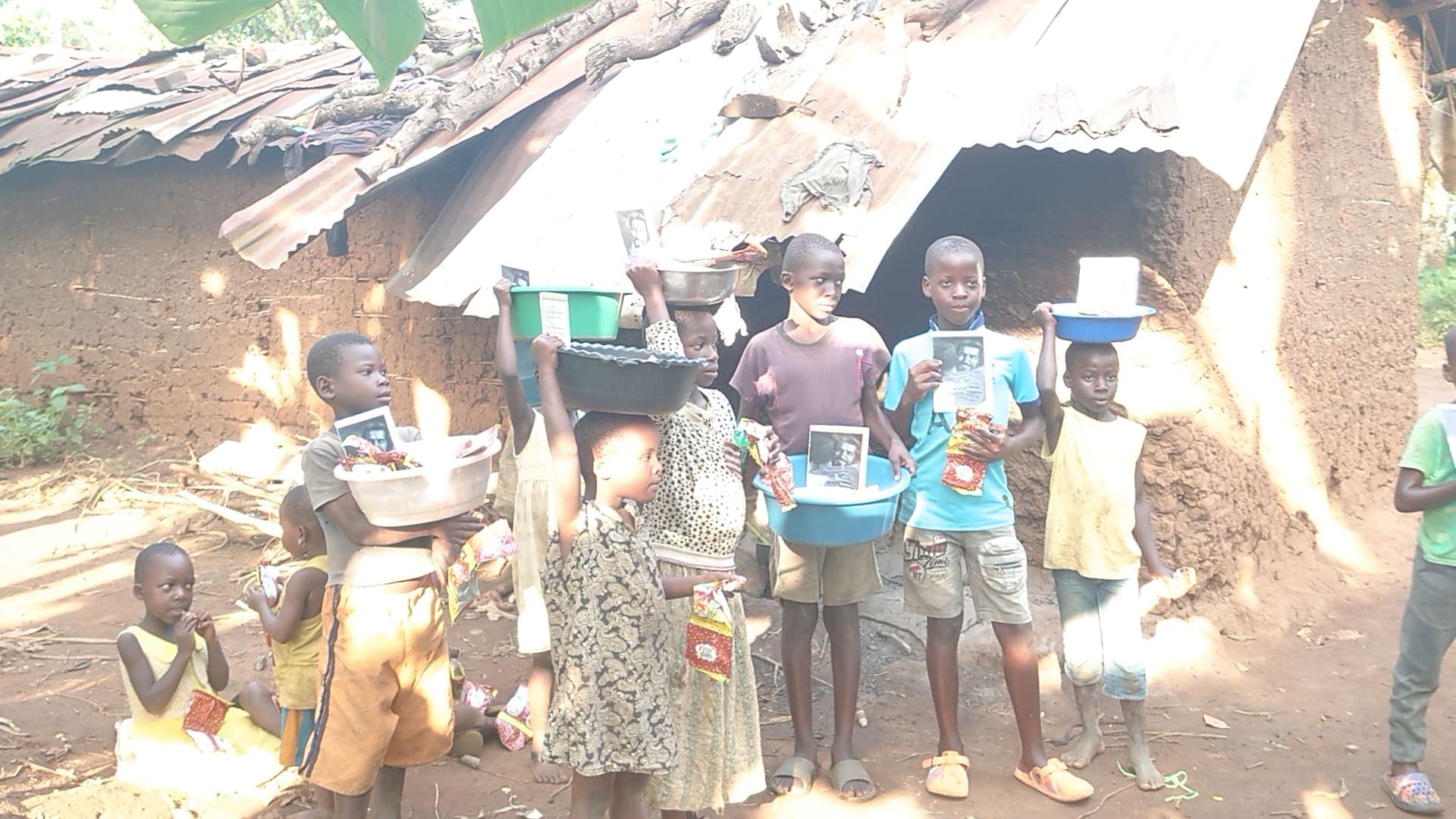 Group of children and adults gathered outside mud houses receiving JFM food gifts.