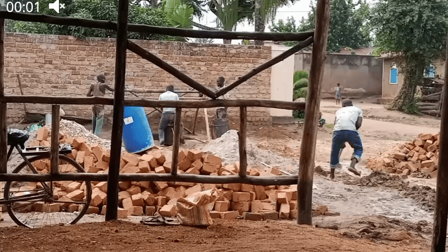 Workers build a water well structure with metal scaffolding inside a brick-walled enclosure.