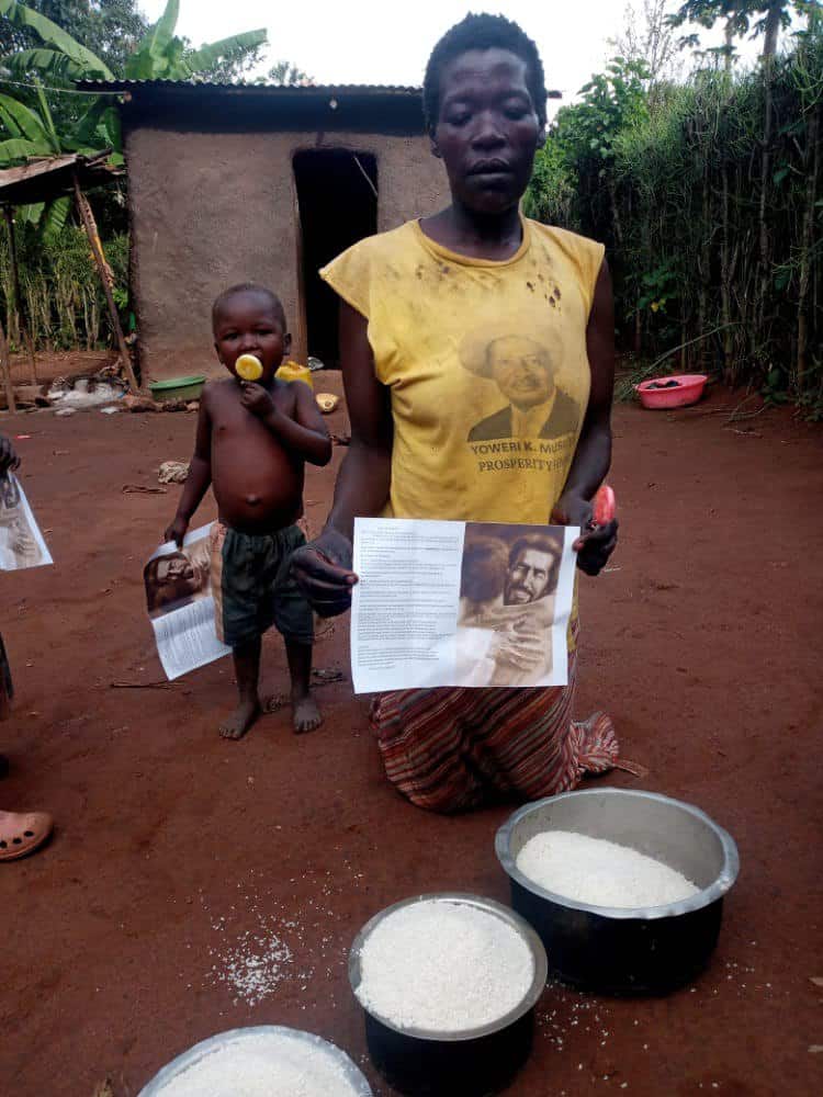 Woman and small child outside a mud house, child holding a food package beside basins of rice and maize.
