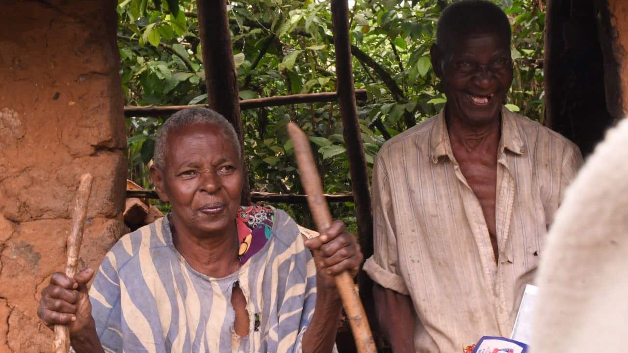 Two elderly men standing together outdoors, one holding a walking stick.