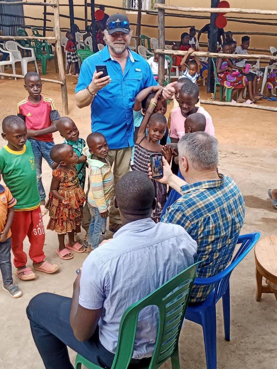 A man in a blue shirt holds up a phone to photograph children gathered on benches at Amazing Grace Church.