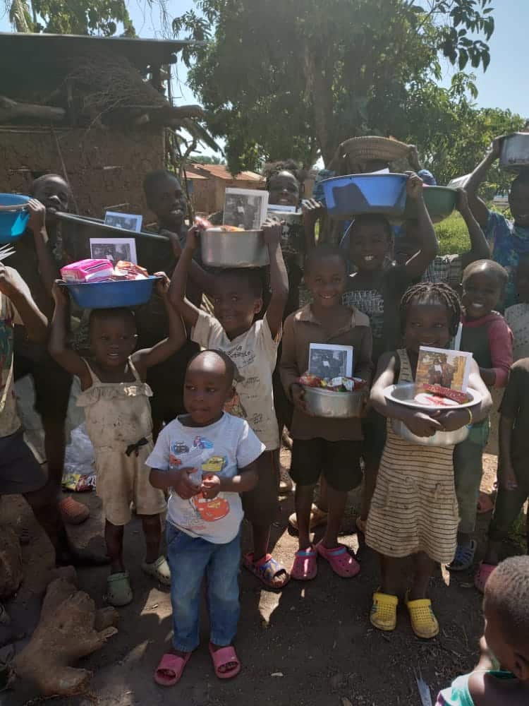 A group of children in bright winter-style knitted hats and clothing stand together at the food and gift distribution in Lelu village.