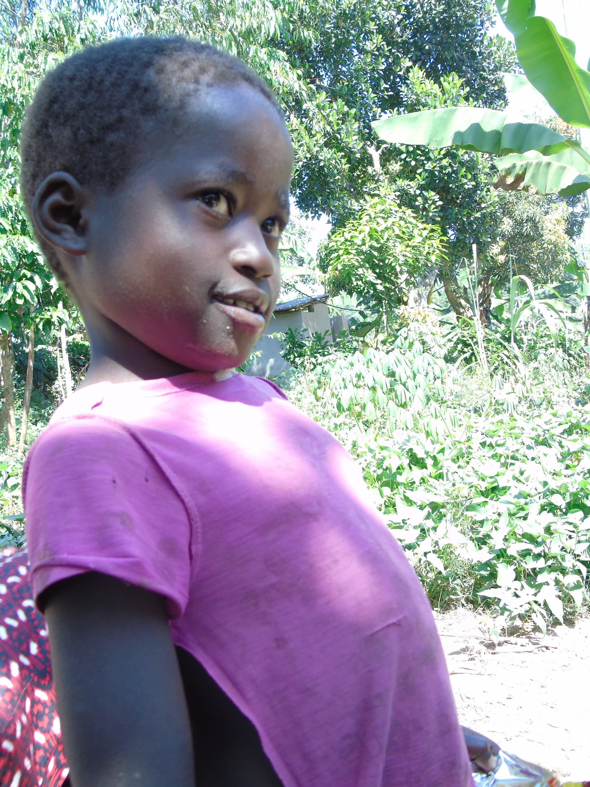 Rotated close-up photo of a young child's face, dressed in purple, outdoors.