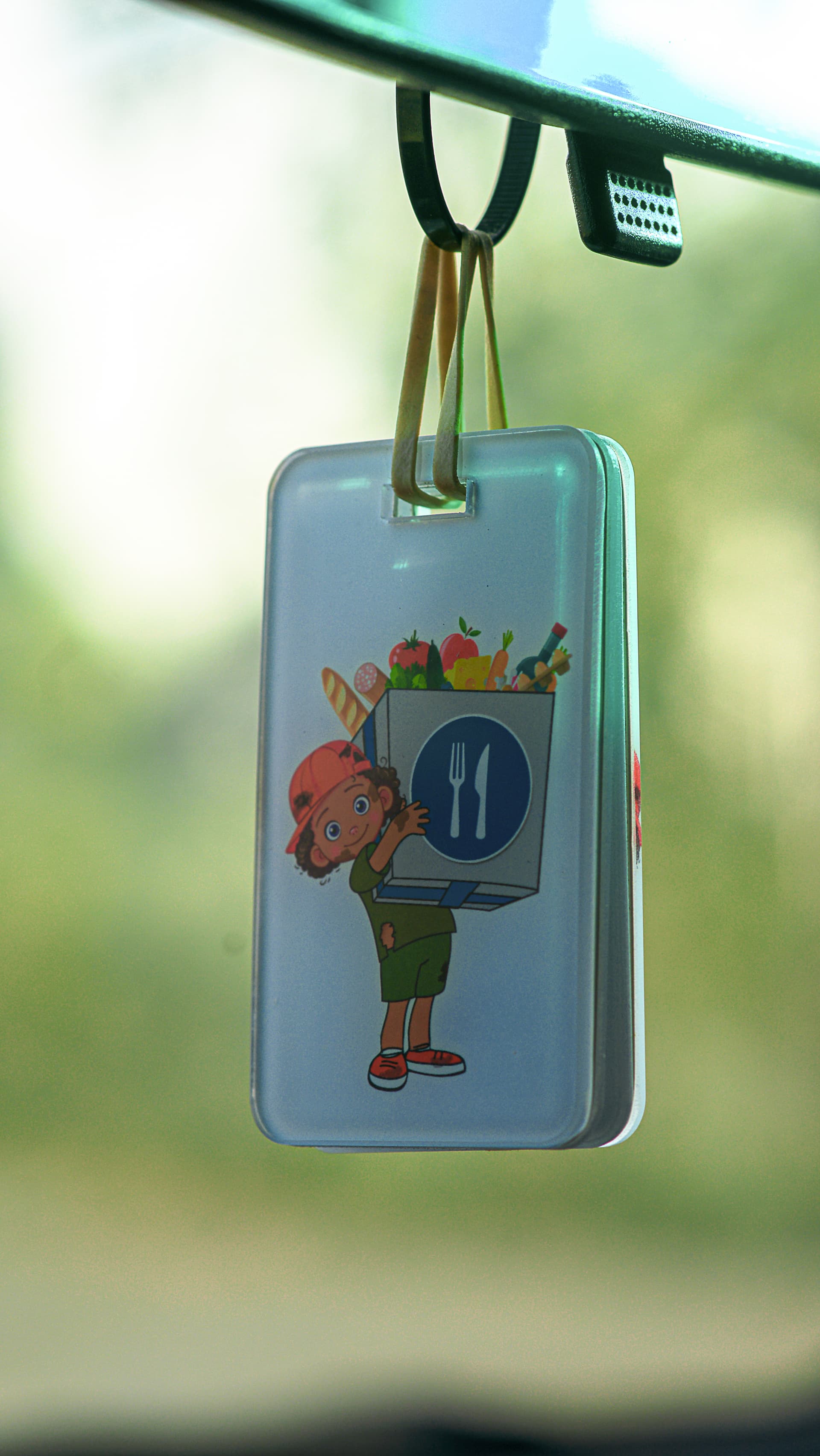 Illustrated air-freshener charm depicting a cartoon chef hangs from a car mirror, not a photo of people.