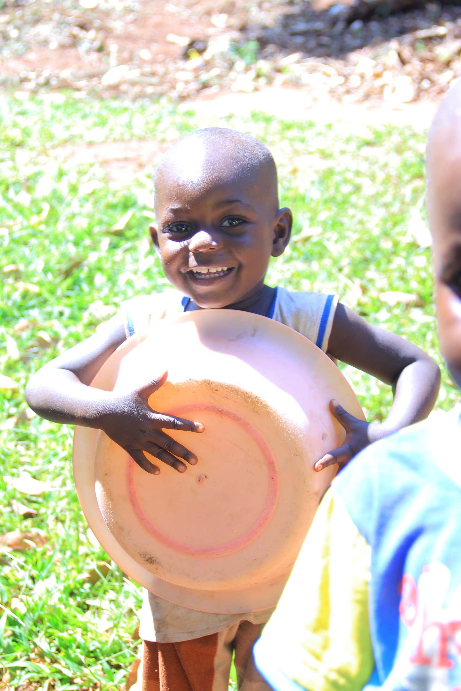 Blurred photo of a boy lifting an orange plastic basin overhead outdoors.