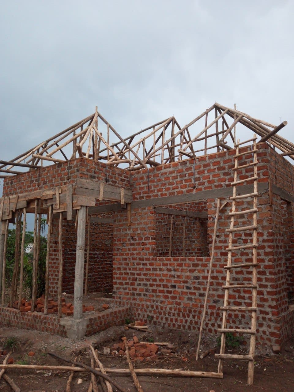 Brick clinic building under construction with exposed roof trusses and a ladder against the wall.