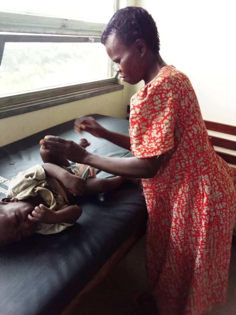Woman in a floral dress examining a swaddled baby on an exam table by a window at Miracle Medical Center.