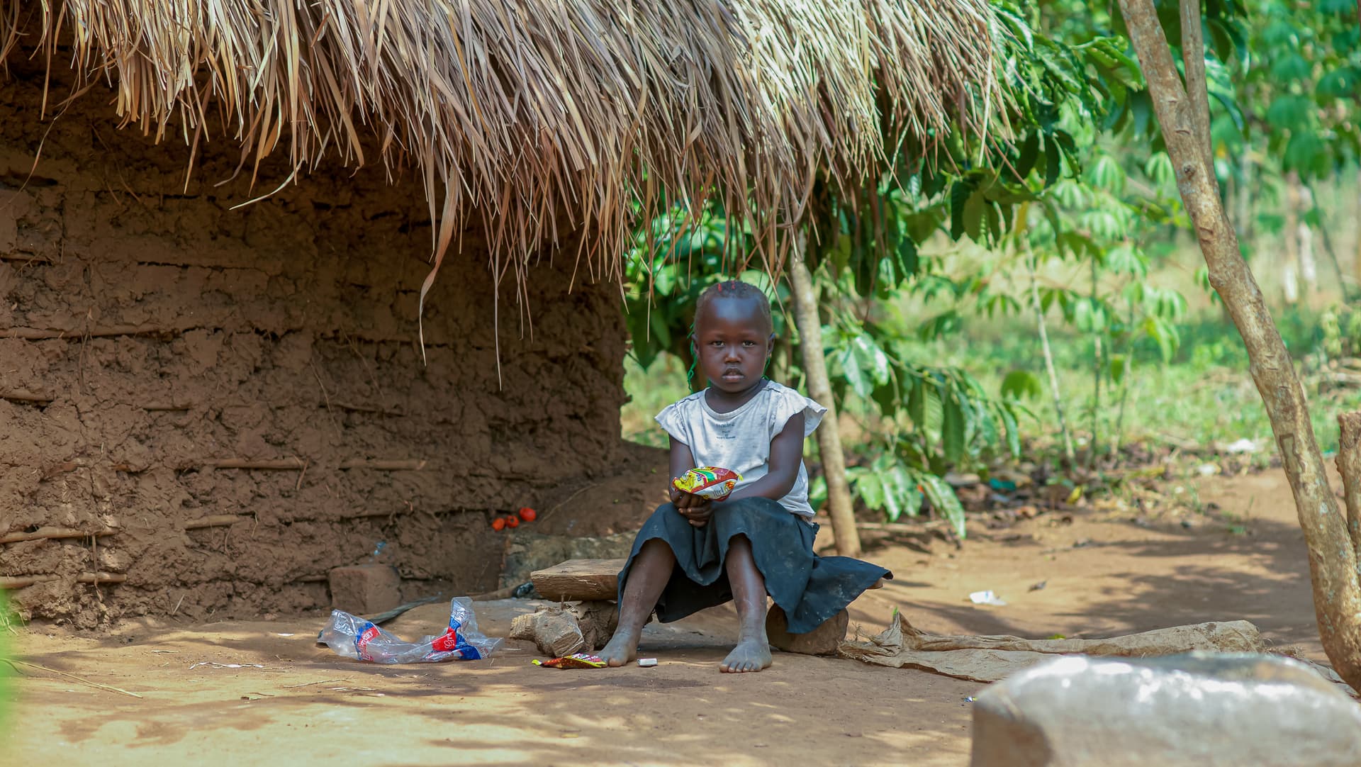 Young girl sits on the ground under a thatched roof, holding an open gospel tract.