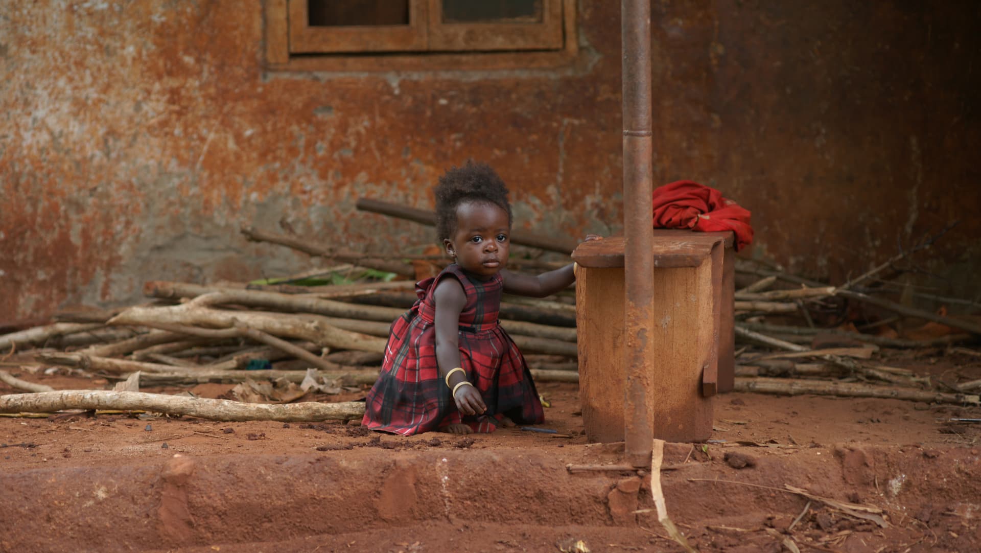 Child sitting on the ground near a pile of firewood, image slightly blurred.