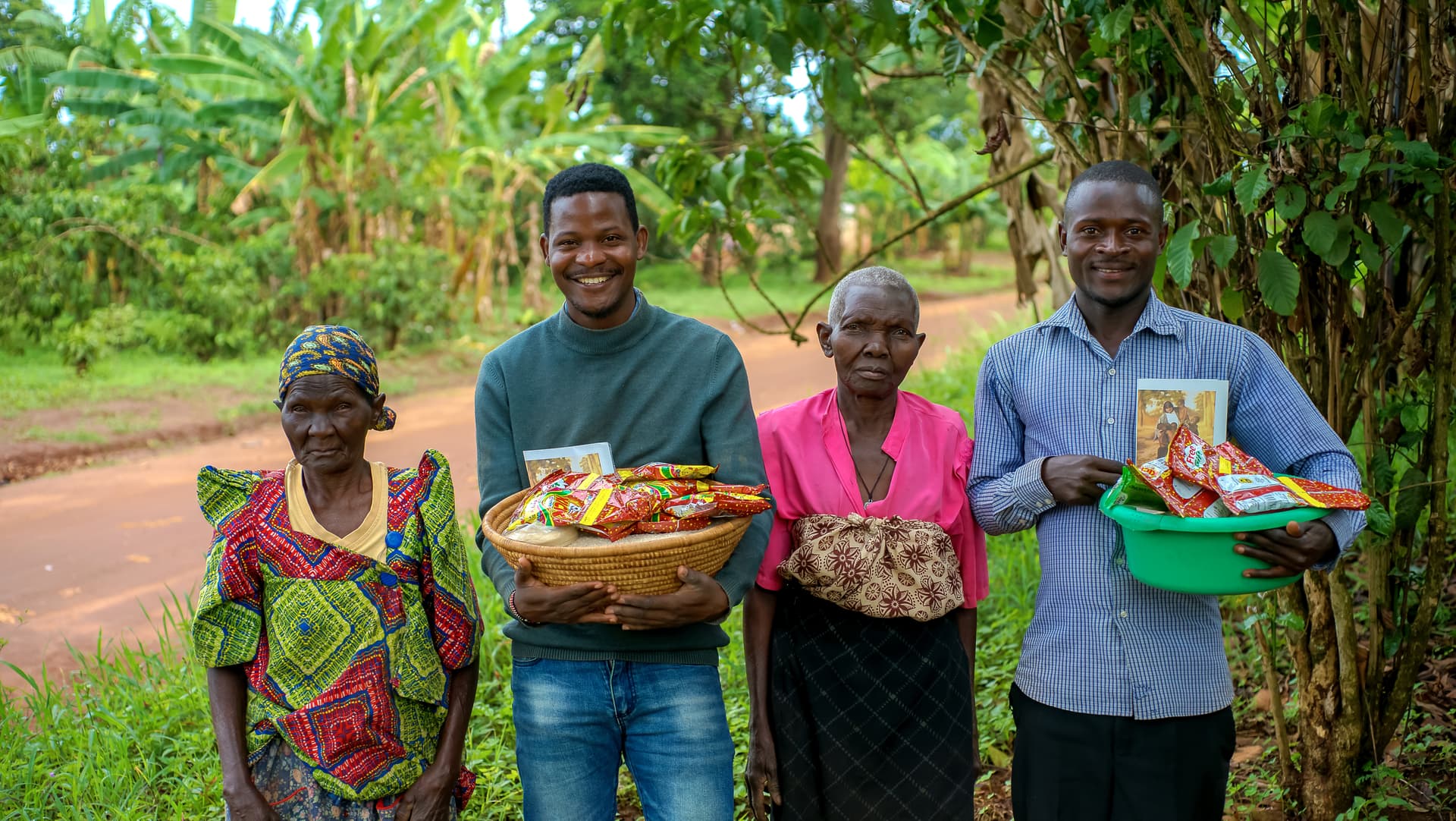Two women and a man standing in a banana grove, each holding a JFM food gift basket.