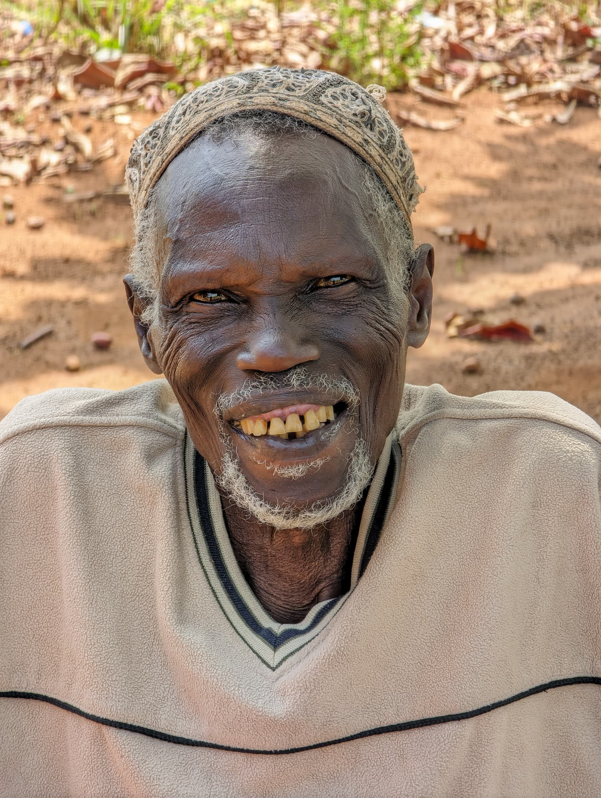 Close portrait of elderly man Mzee Ssebunya in a knit cap, smiling broadly.