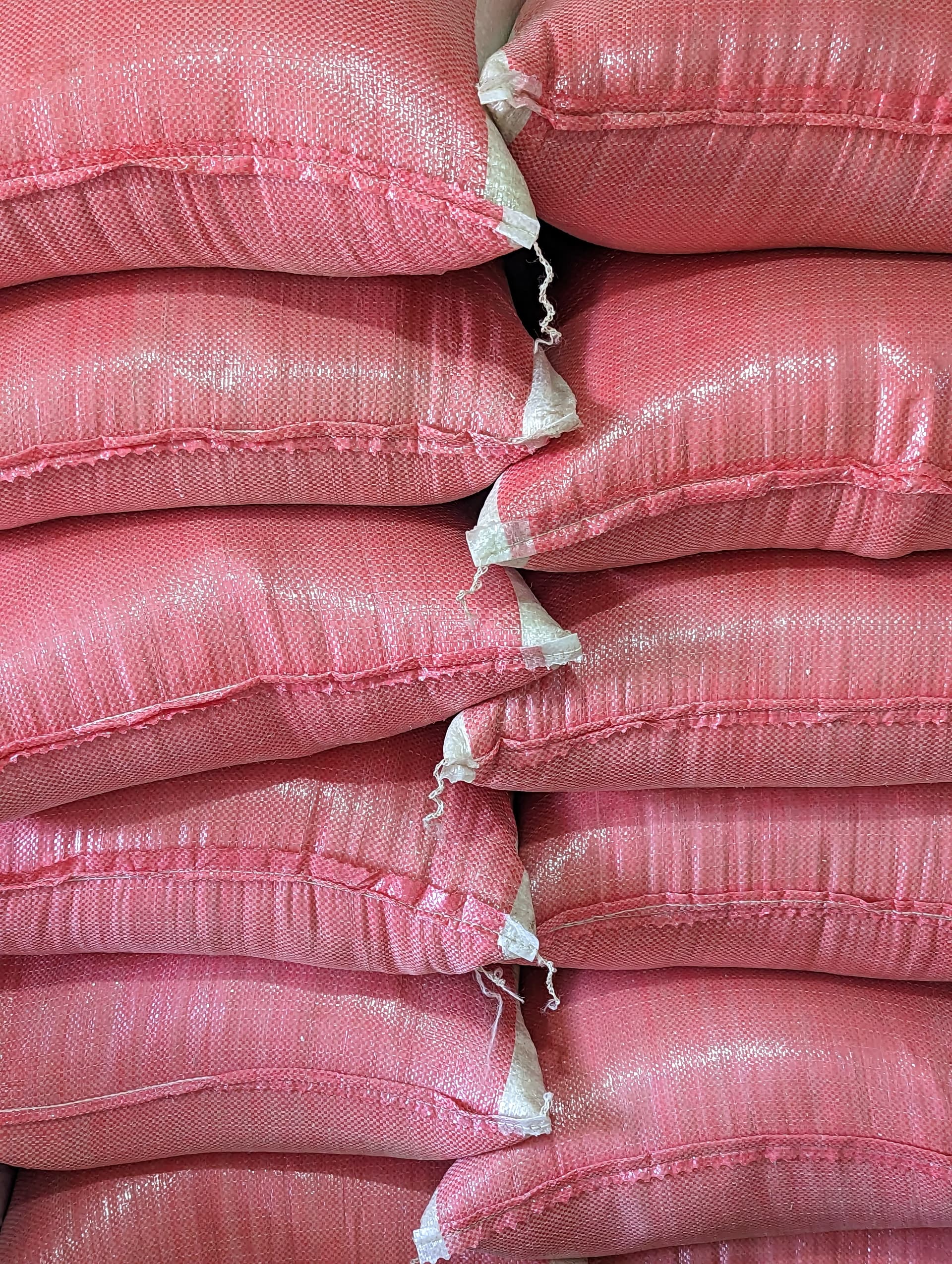 Stack of pink woven polypropylene sacks, likely rice or maize, piled for distribution.