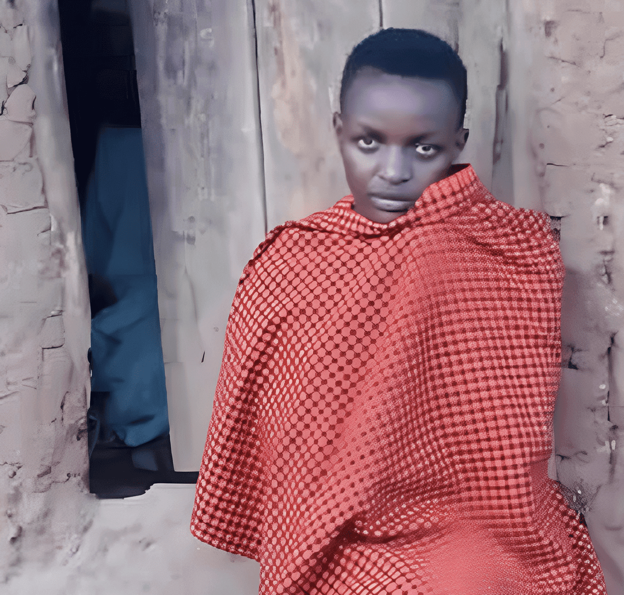 Young woman wrapped in a red plaid blanket standing in a doorway, part of Mary Gloria's story at Miracle Medical Center.