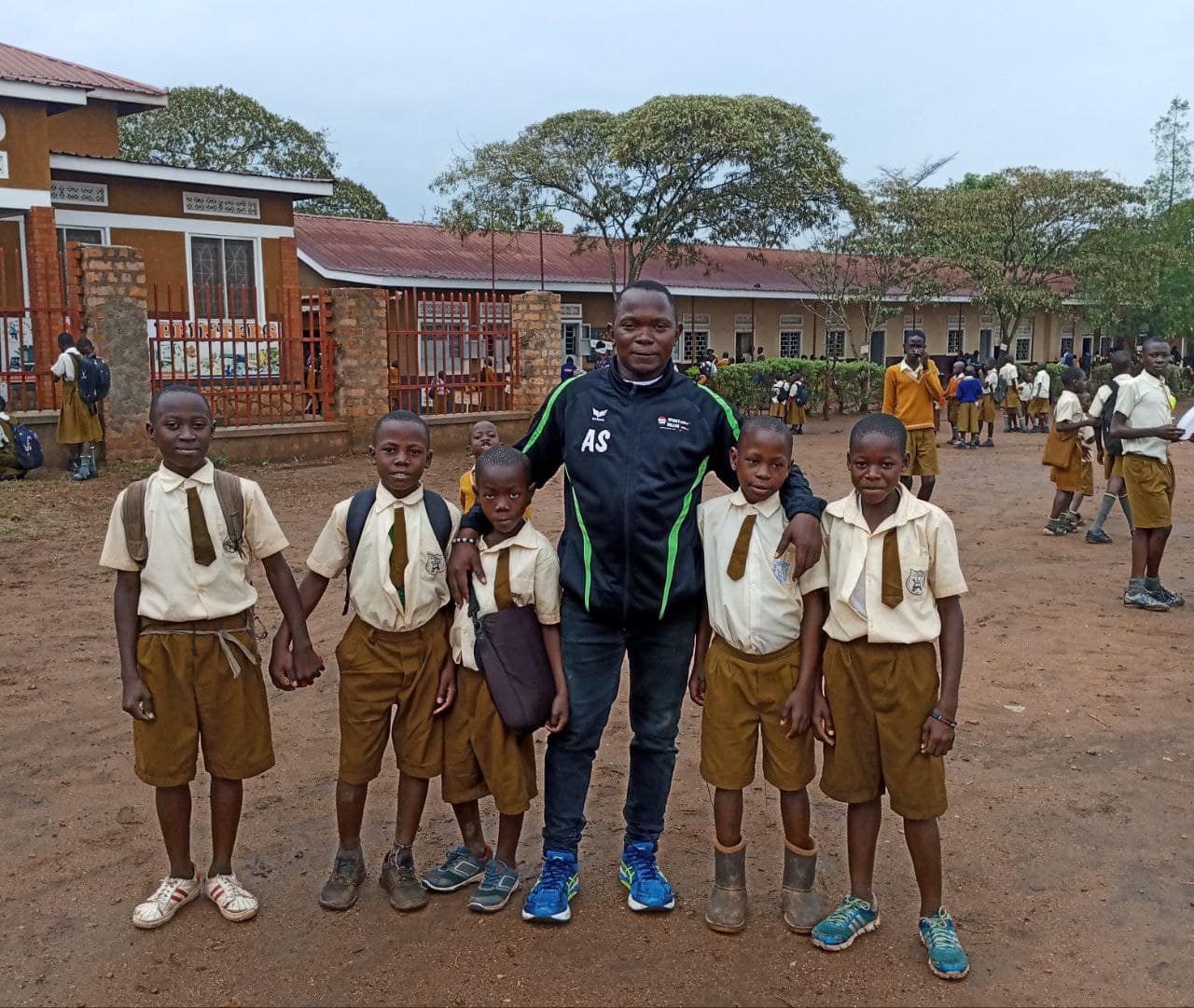 Man standing with a group of schoolboys in uniform on a school compound.