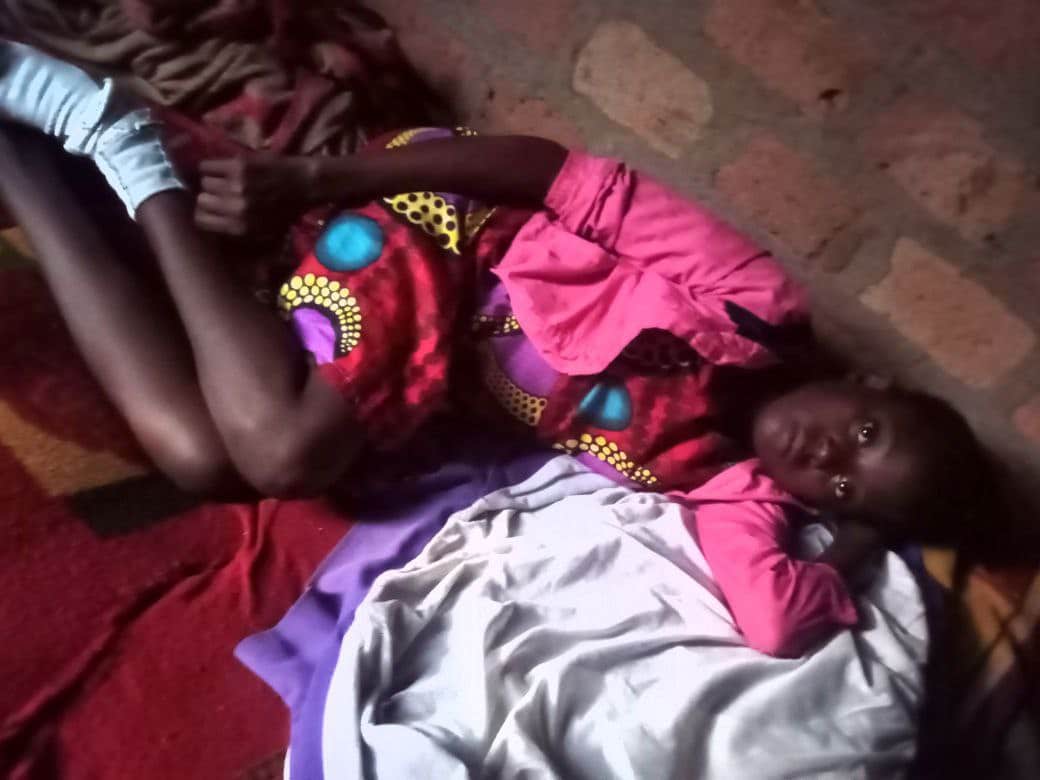 Blurry photo of a person lying down wrapped in colorful blankets near a brick wall, likely Betty resting at Mashariki Children's Home.