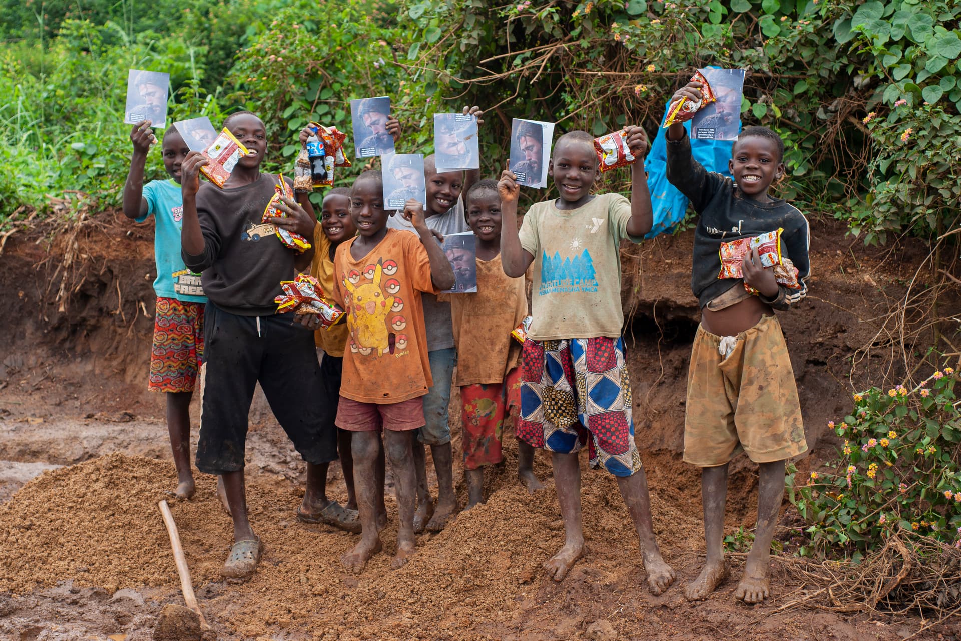 A group of people and children stand outdoors holding up photo cards.